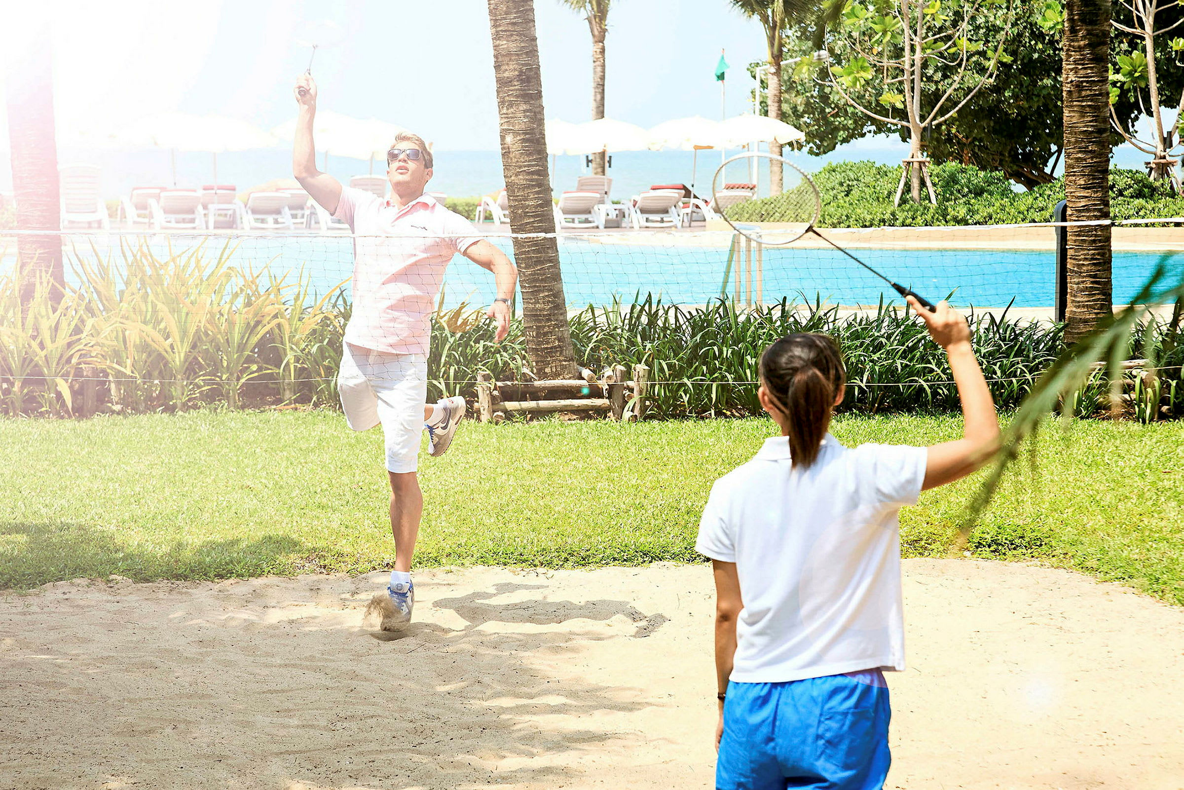 Två människor spelar badminton på en gräsplan med en pool i bakgrunden. (AI-genererad text)