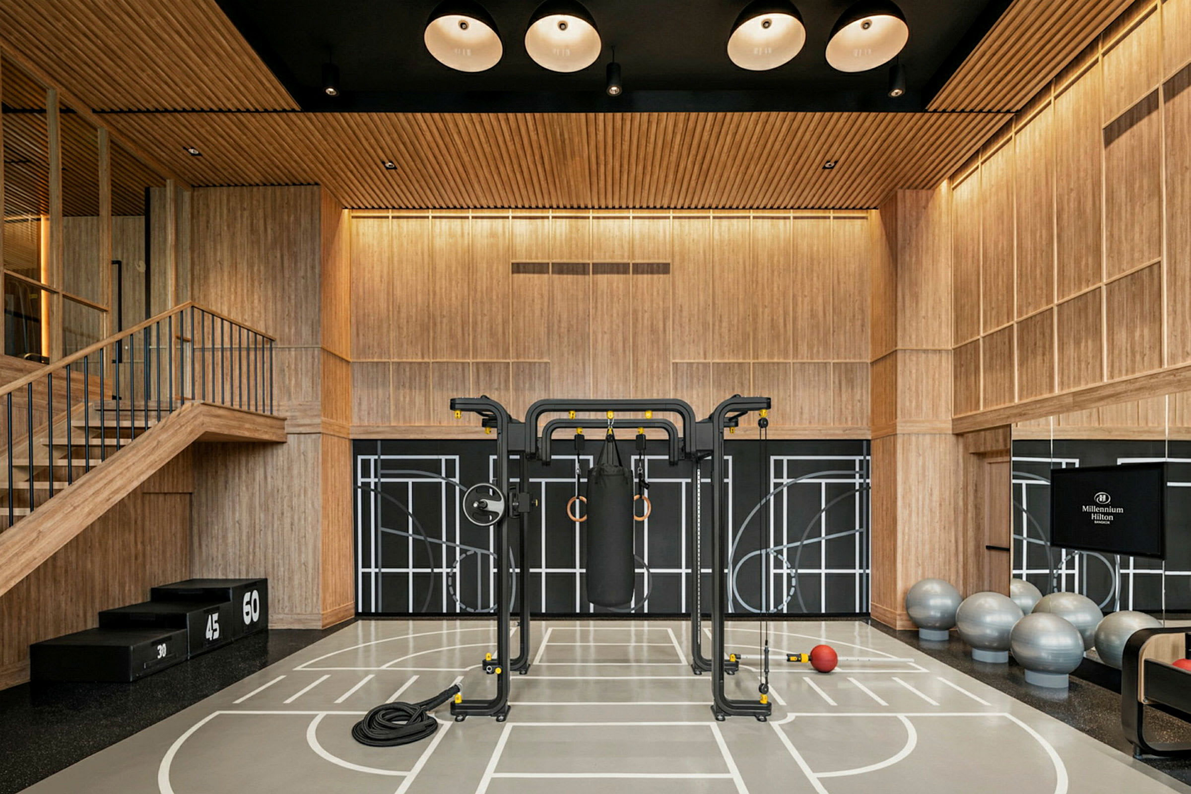 Ett gym med träpaneler och träningsutrustning inklusive gymbollar, en boxsäck och ett räcke. (AI-genererad text)