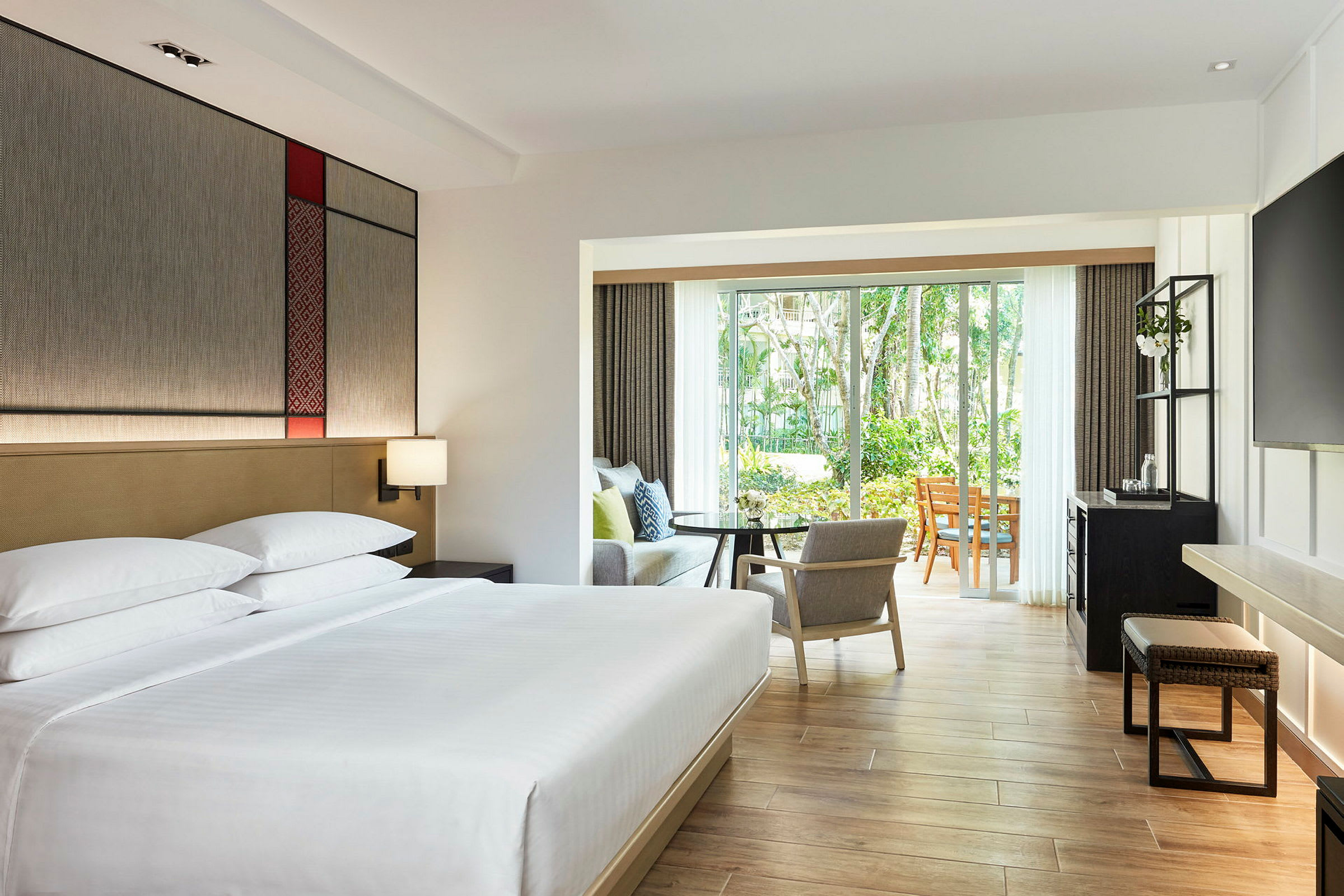 Ett modernt hotellrum med en stor säng, sittgrupp och glasdörrar som leder ut till en grönskande trädgård. (AI-genererad text)