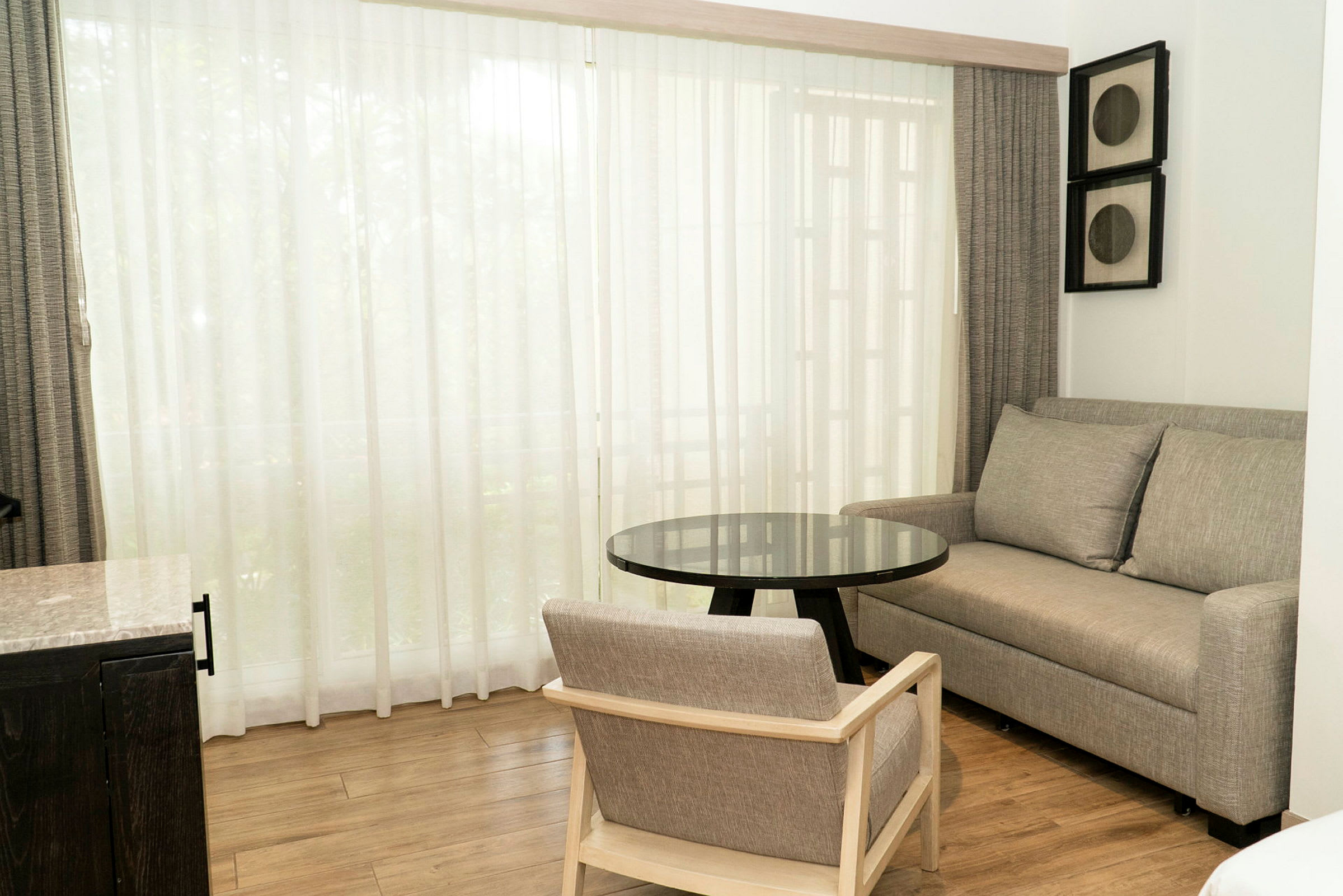 Ett rum med en soffa och en stol i grått, en svart glasbord och ett stort fönster med vita gardiner. (AI-genererad text)