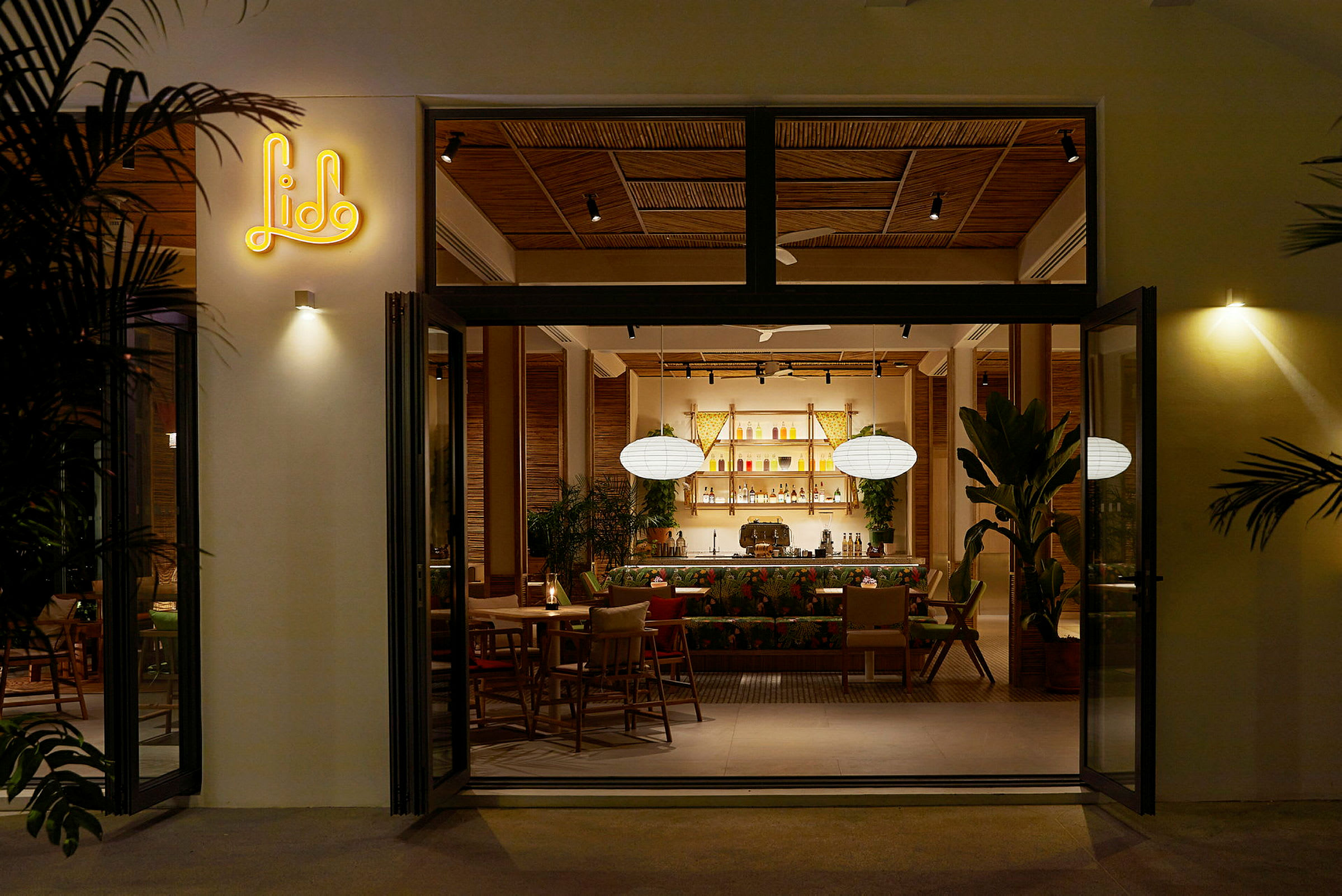 En öppen dörr till en restaurang med modern inredning, där insidan har växter och en upplyst bardisk. (AI-genererad text)