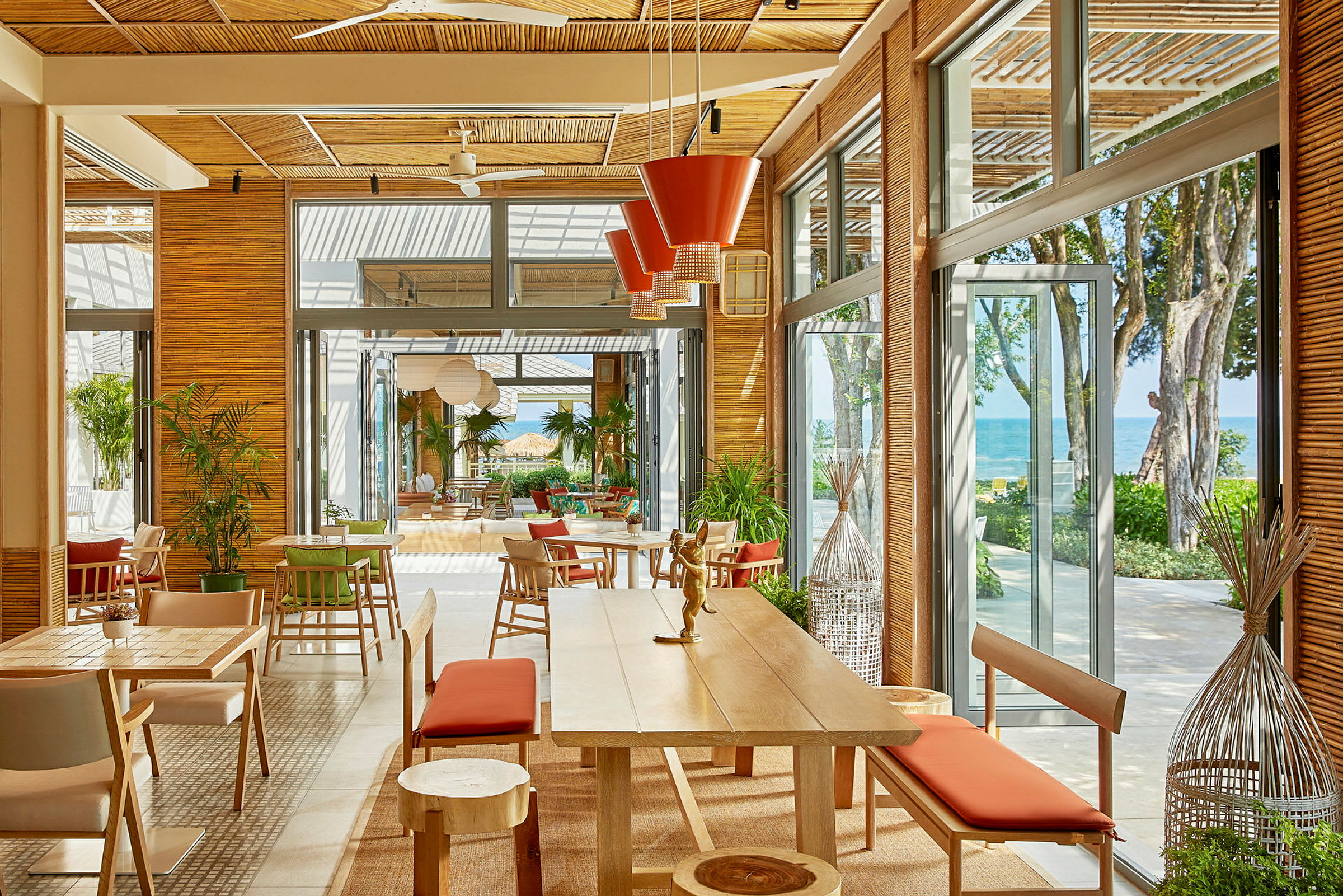 En ljus och rymlig restaurang med stora fönster och utsikt mot havet. Möbeln är modern med träslag och röda detaljer. (AI-genererad text)