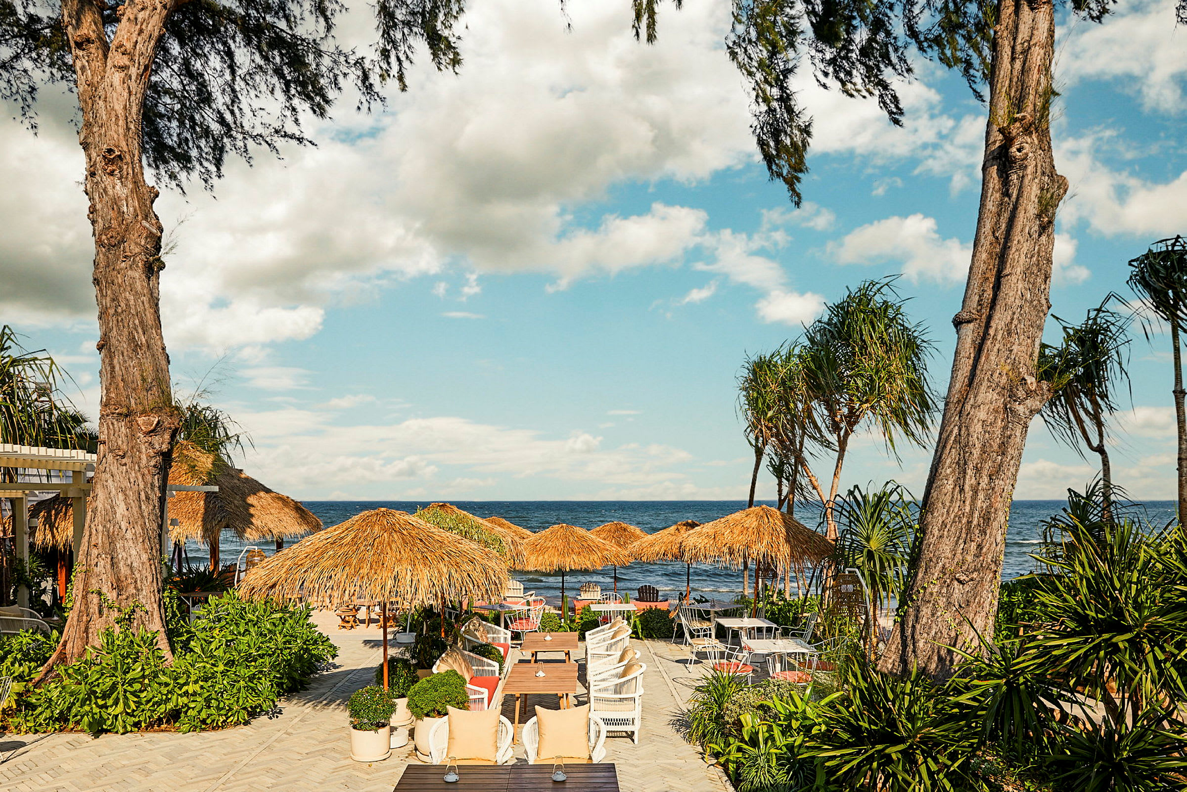 Strandnära restaurang med sittplatser och parasoller i tropisk miljö. (AI-genererad text)