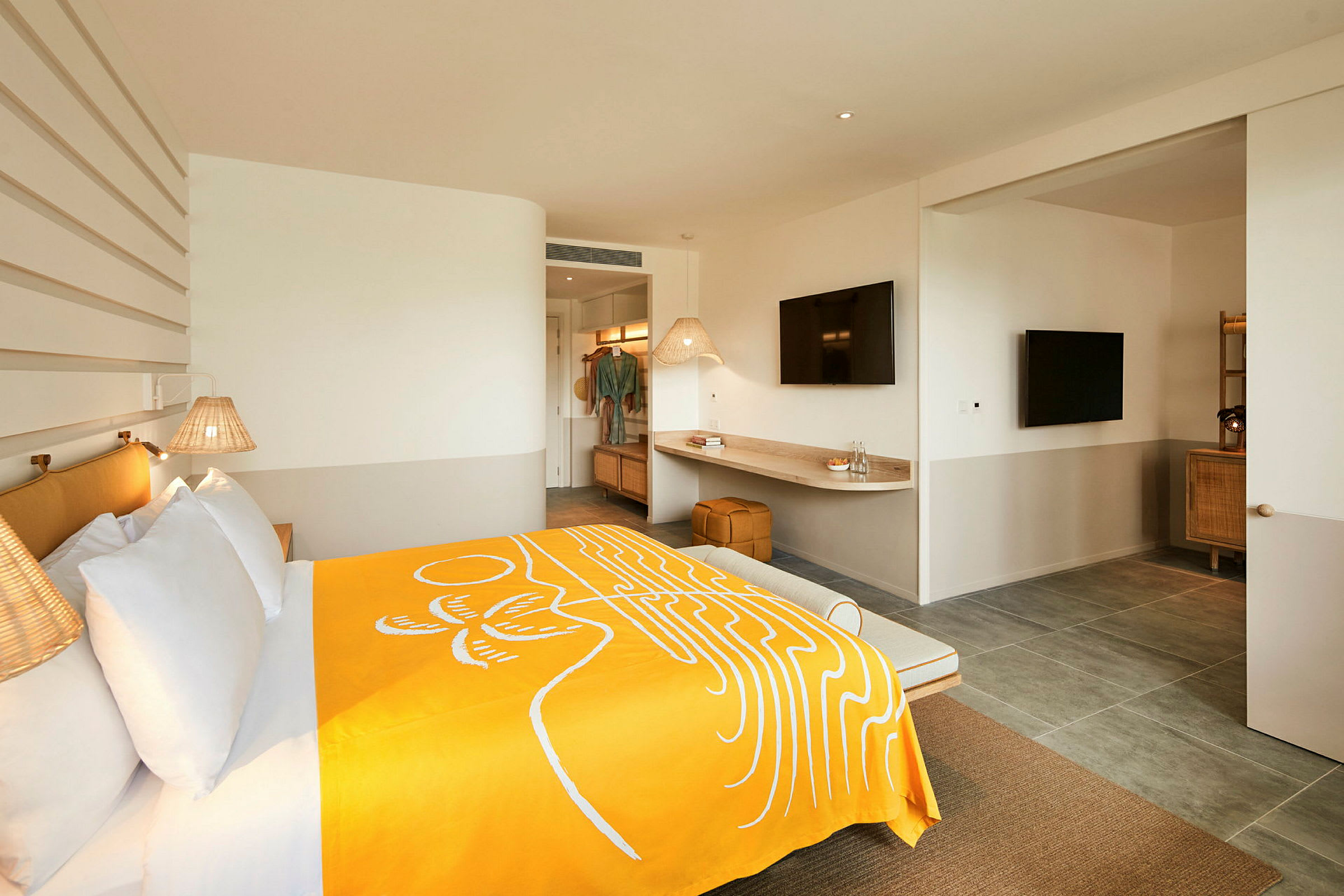 Ett modernt hotellrum med en bred säng täckt med ett gult täcke, väggmonterade lampor och en skrivbordsyta med en TV ovanför. (AI-genererad text)
