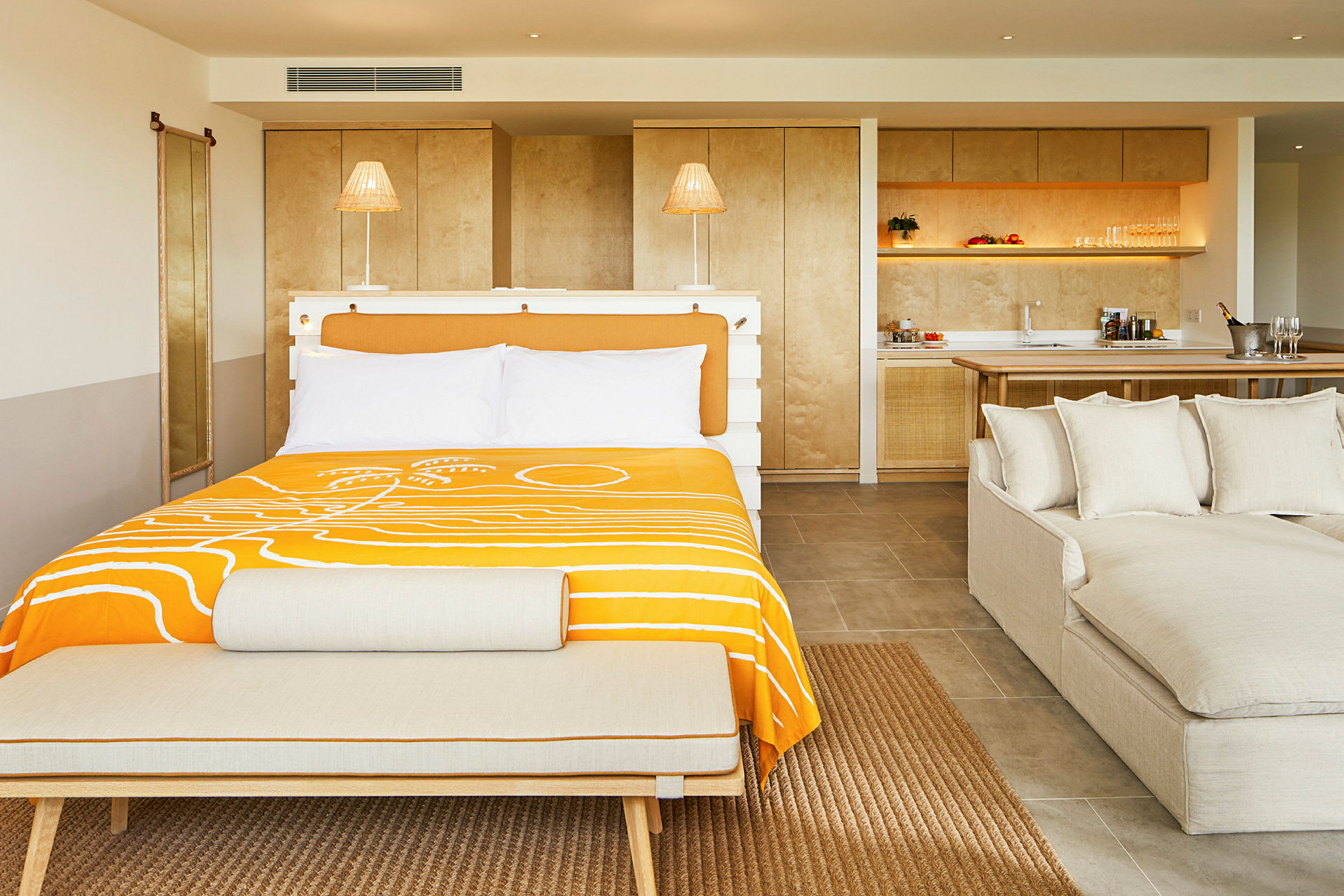 Ett hotellrum med en dubbelsäng klädd med orange sängkläder, en soffa och ett köksområde i bakgrunden. (AI-genererad text)
