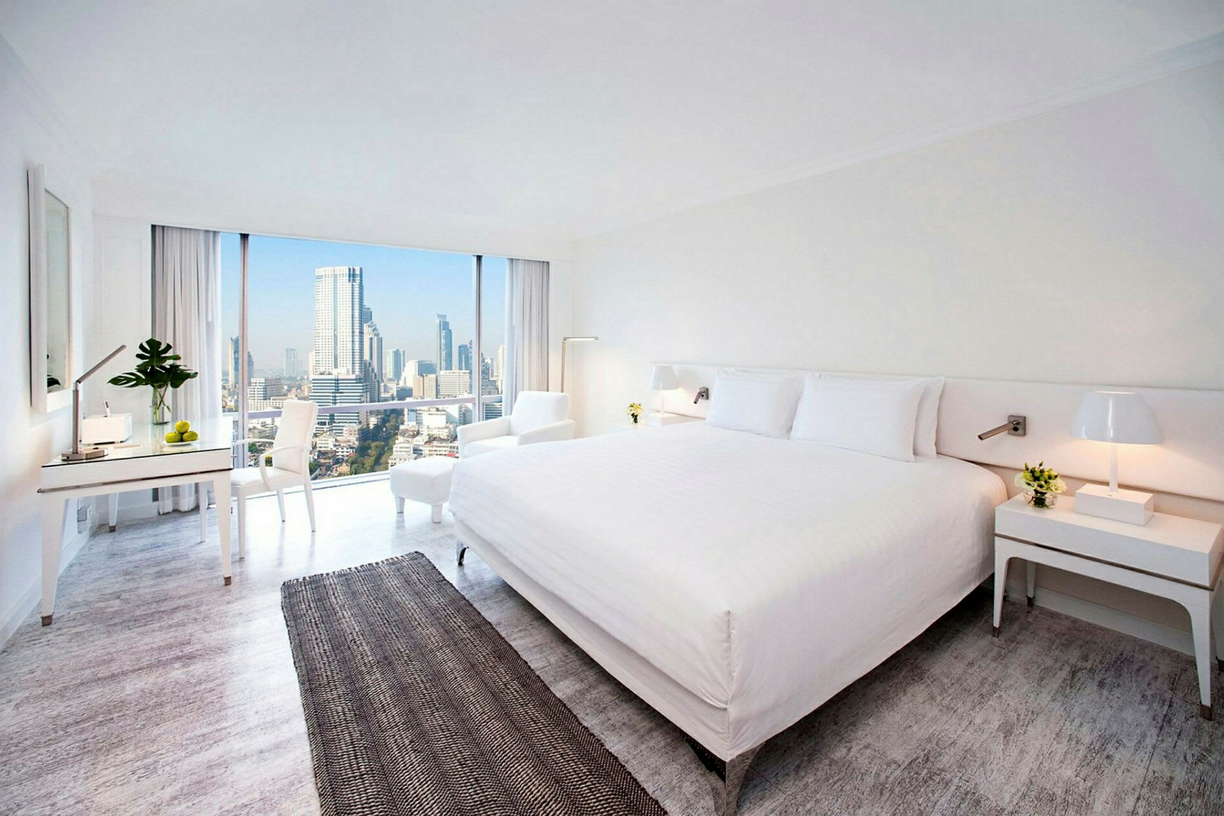 Hotellrum med modern inredning, stor säng och utsikt över stadssilhuetten genom stora fönster. (AI-genererad text)