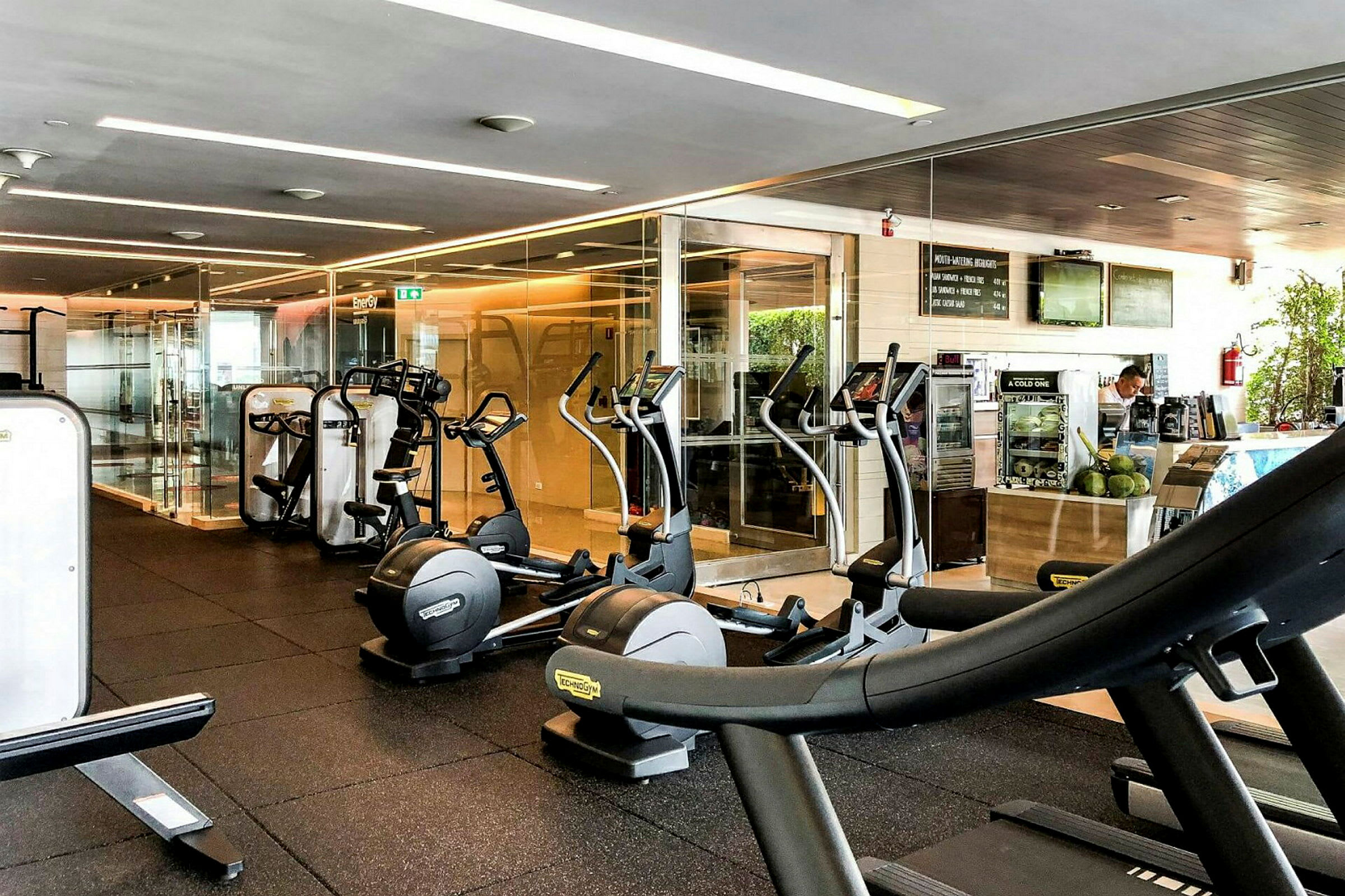 Ett gym med träningsutrustning som löpband och crosstrainers, samt en liten barsdisk i bakgrunden. (AI-genererad text)