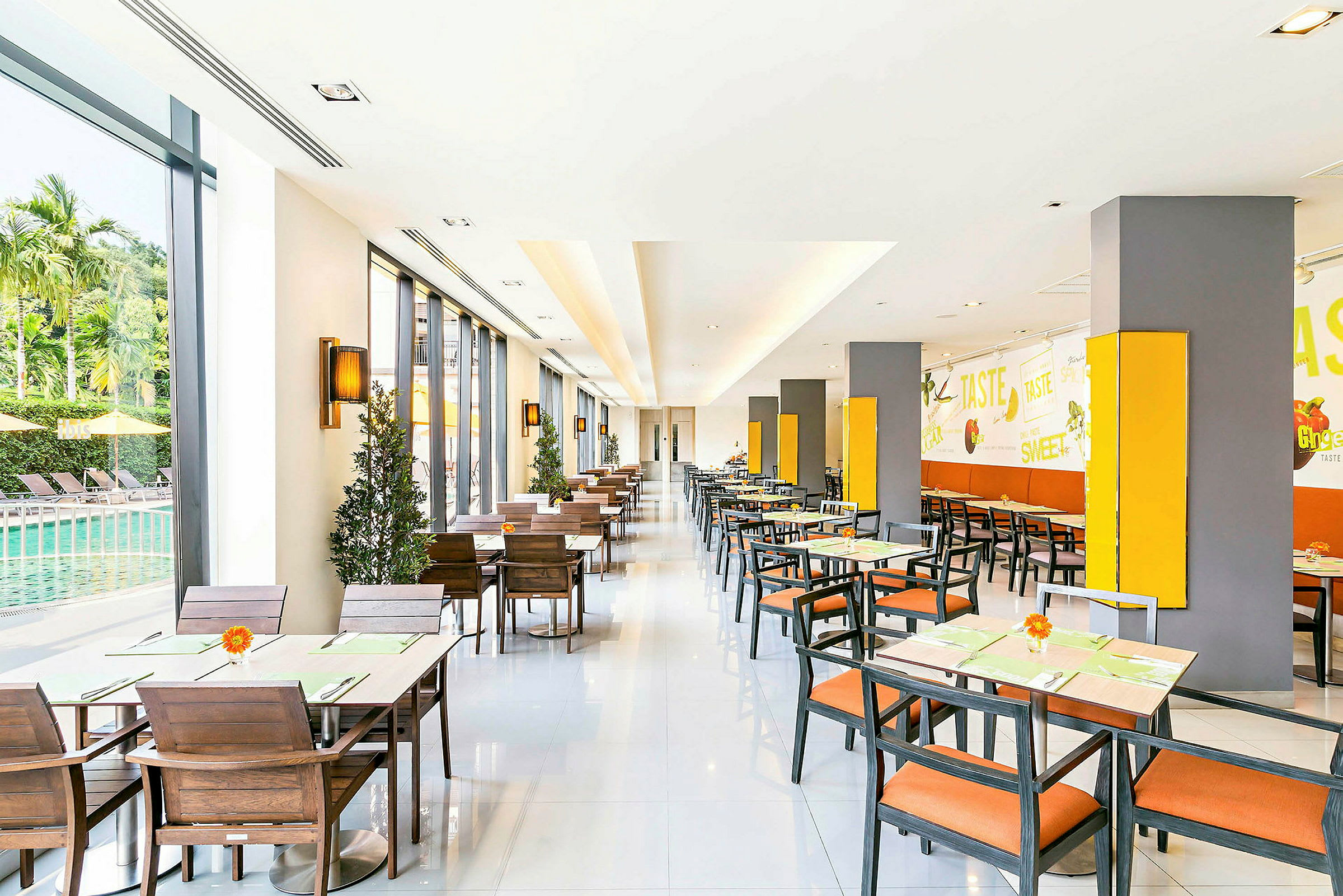 En ljus restaurang med sittplatser, fönster mot en pool och väggdekorationer. (AI-genererad text)