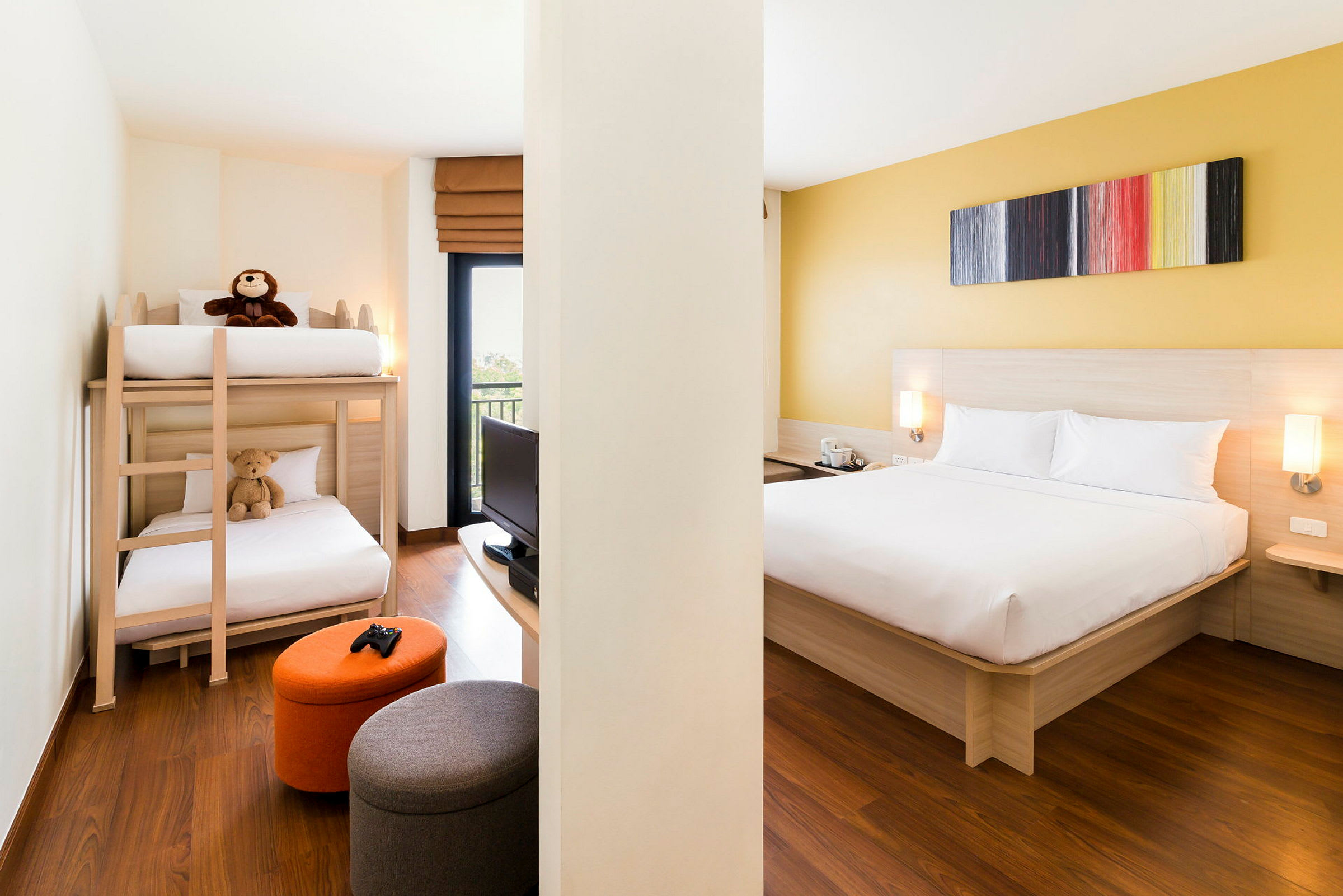 Ett hotellrum med en våningssäng, dubbelsäng, liten TV och sittpuffar. (AI-genererad text)
