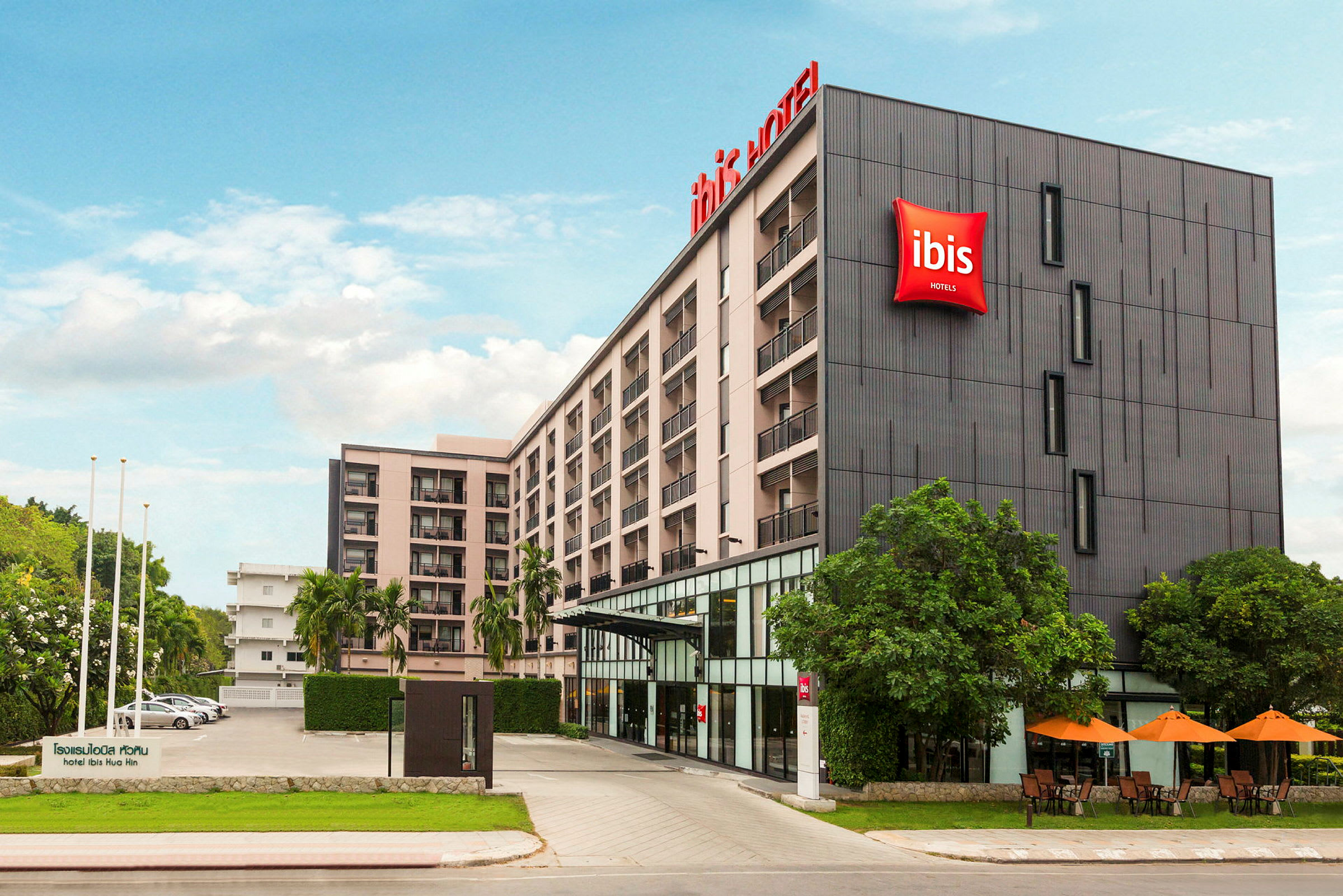 Bild på fasaden av ett flervåningshotell med hotellskylt och omgivande grönska. (AI-genererad text)