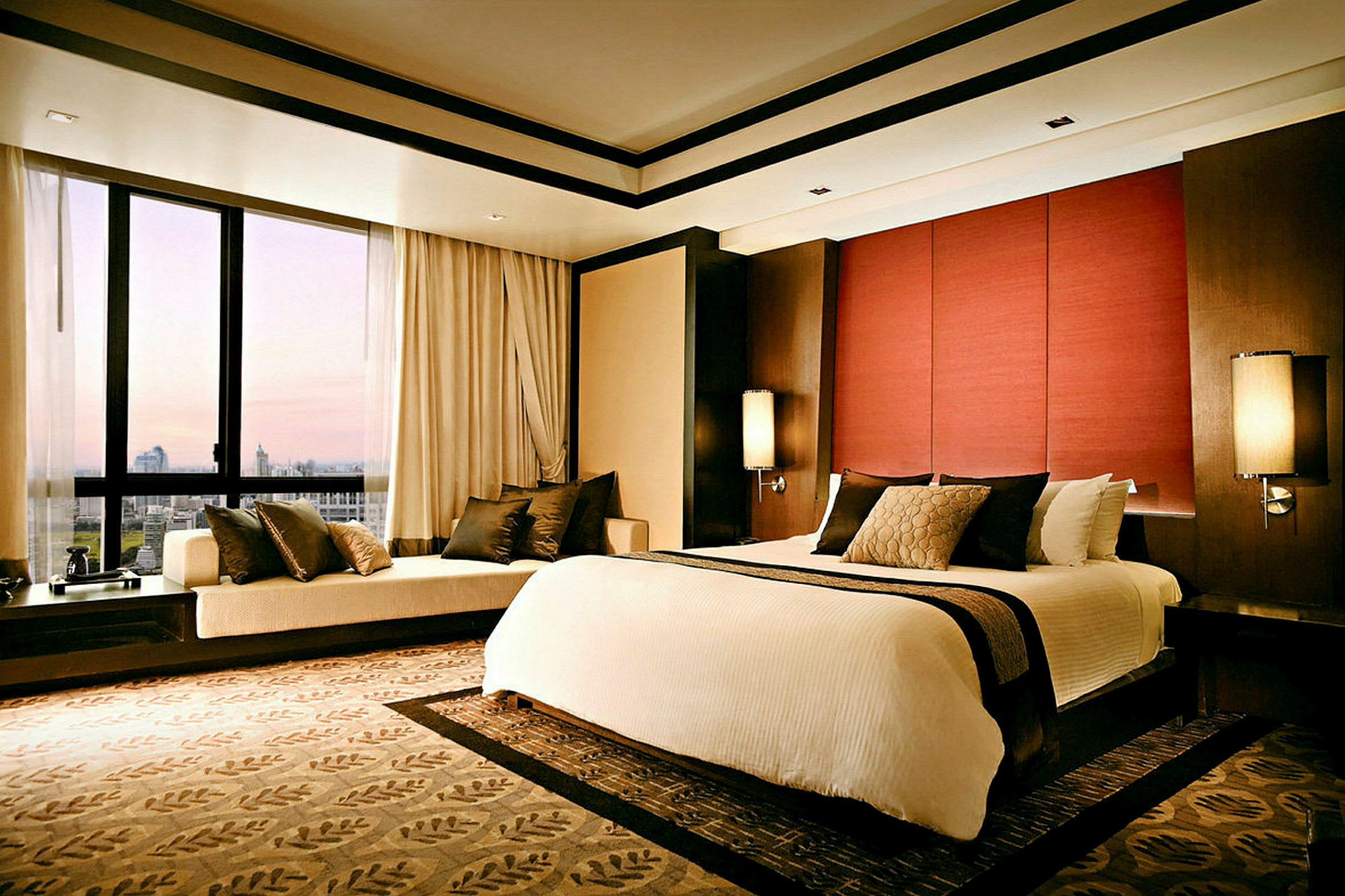 Ett elegant hotellrum med en stor säng dekorerad med kuddar och täcke, en sittgrupp vid fönstret och modern belysning. (AI-genererad text)