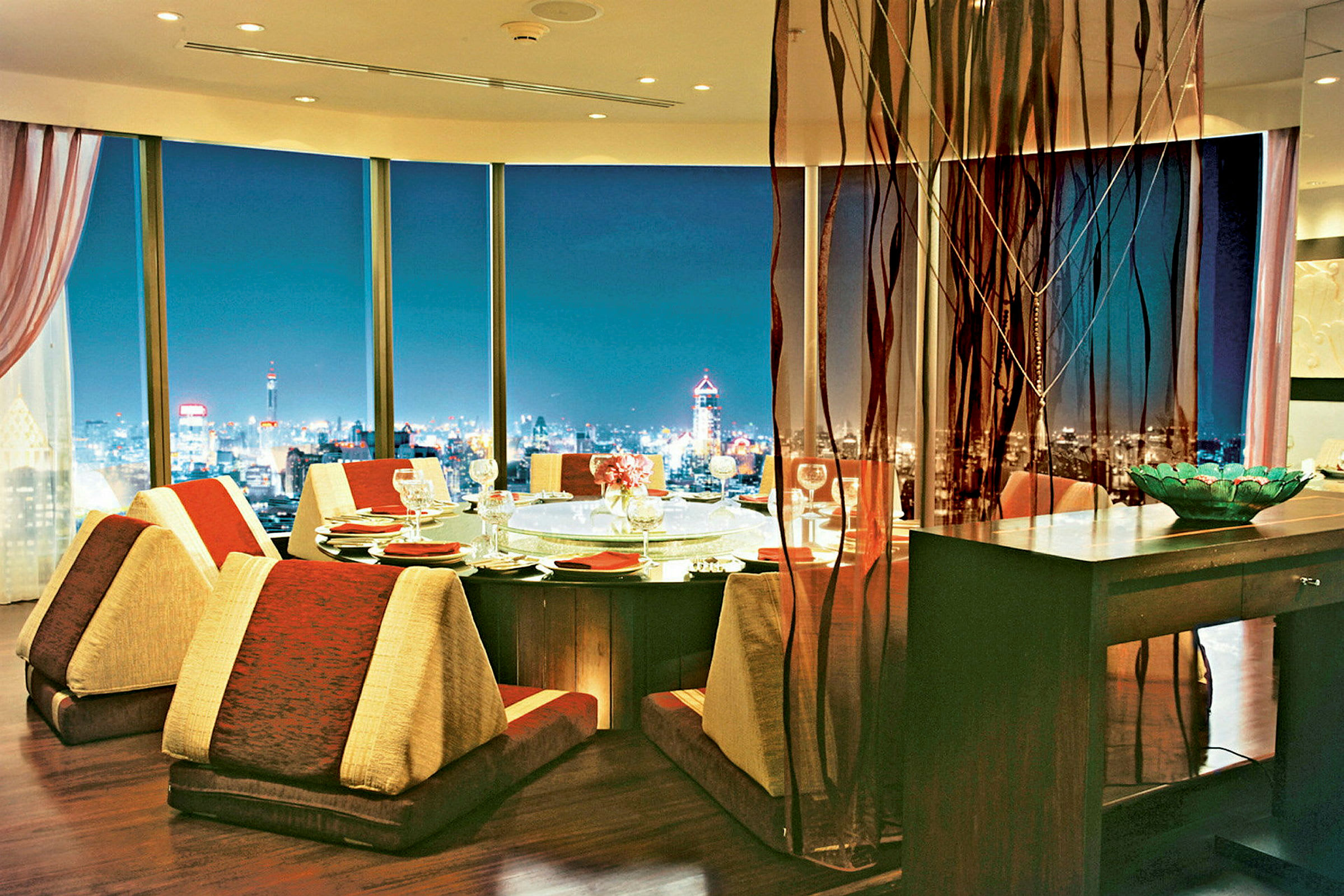 En elegant matsal med panoramautsikt över en upplyst stad på kvällen. (AI-genererad text)