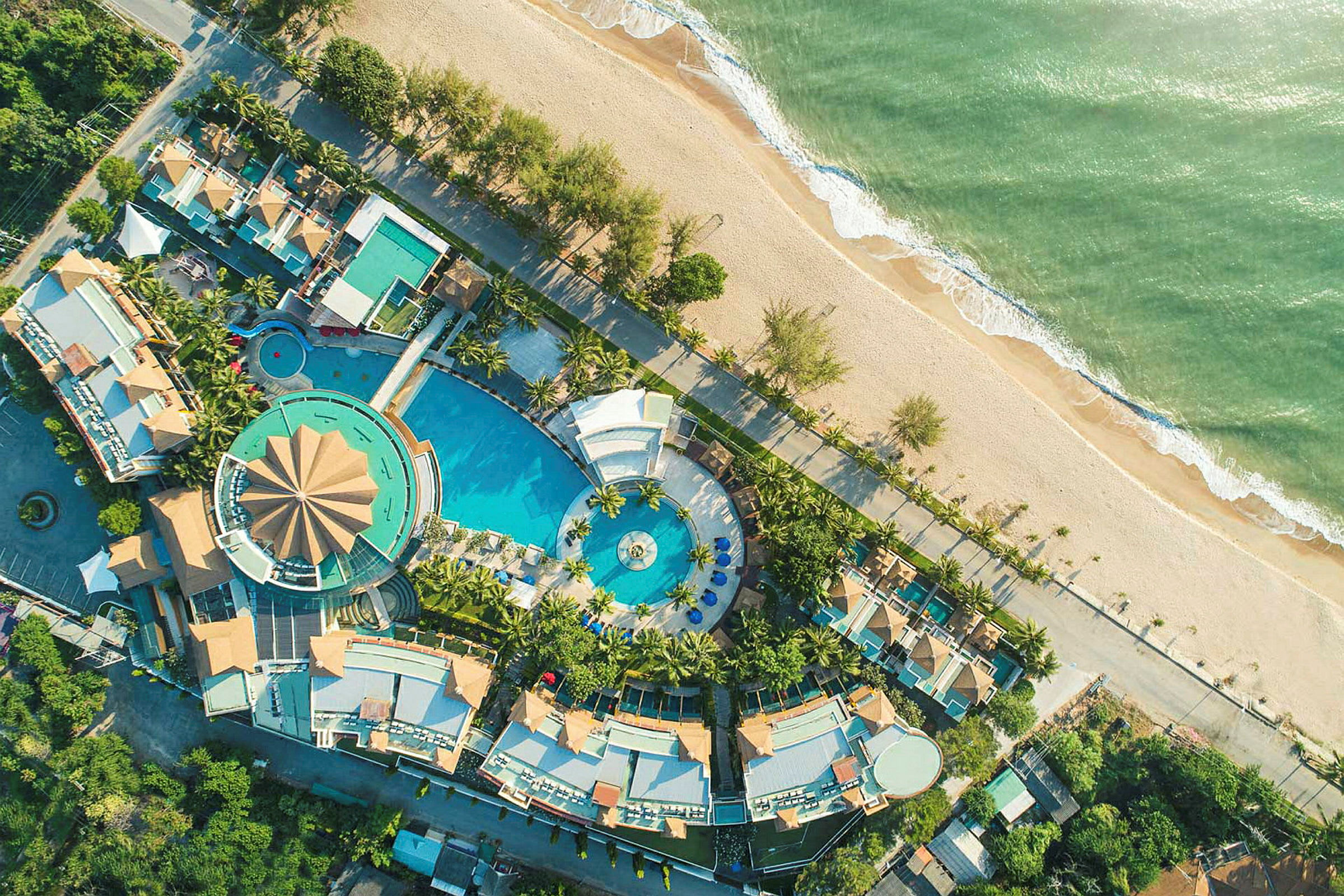 Flygfoto av en resort med poolområde och omgivande byggnader vid stranden. (AI-genererad text)
