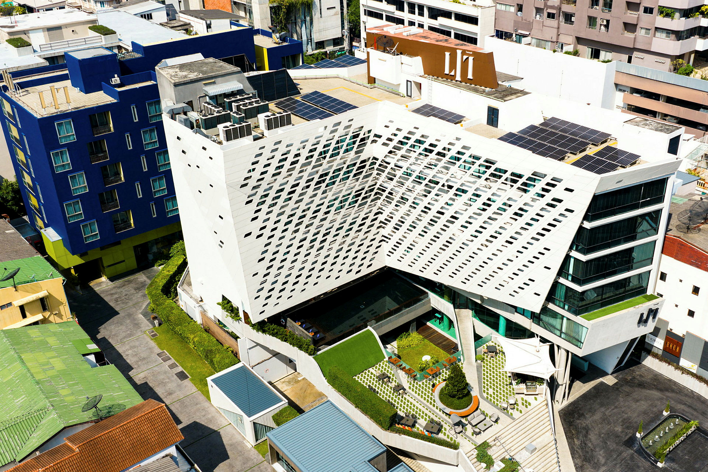 Flygfoto av en modern byggnad med geometrisk arkitektur, omgiven av andra byggnader. (AI-genererad text)