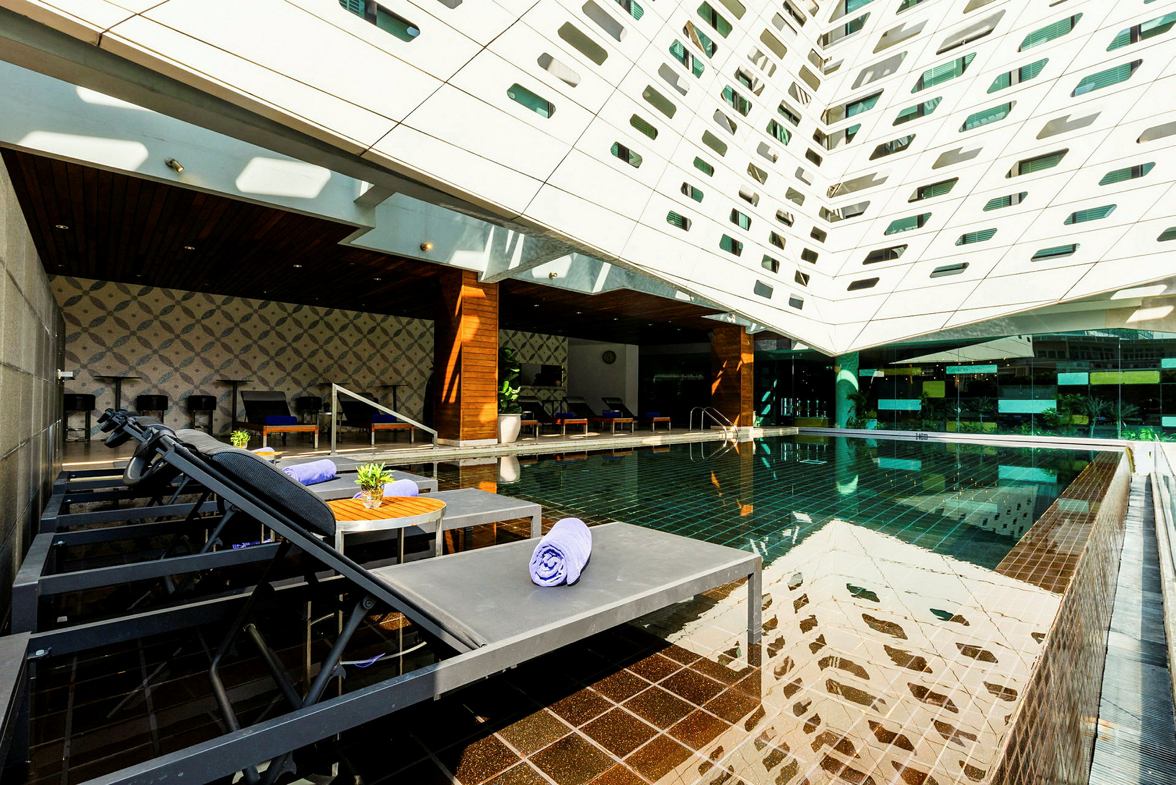 Ett modernt utomhusområde med en pool, solstolar och ett tak täckt av geometriska öppningar. (AI-genererad text)