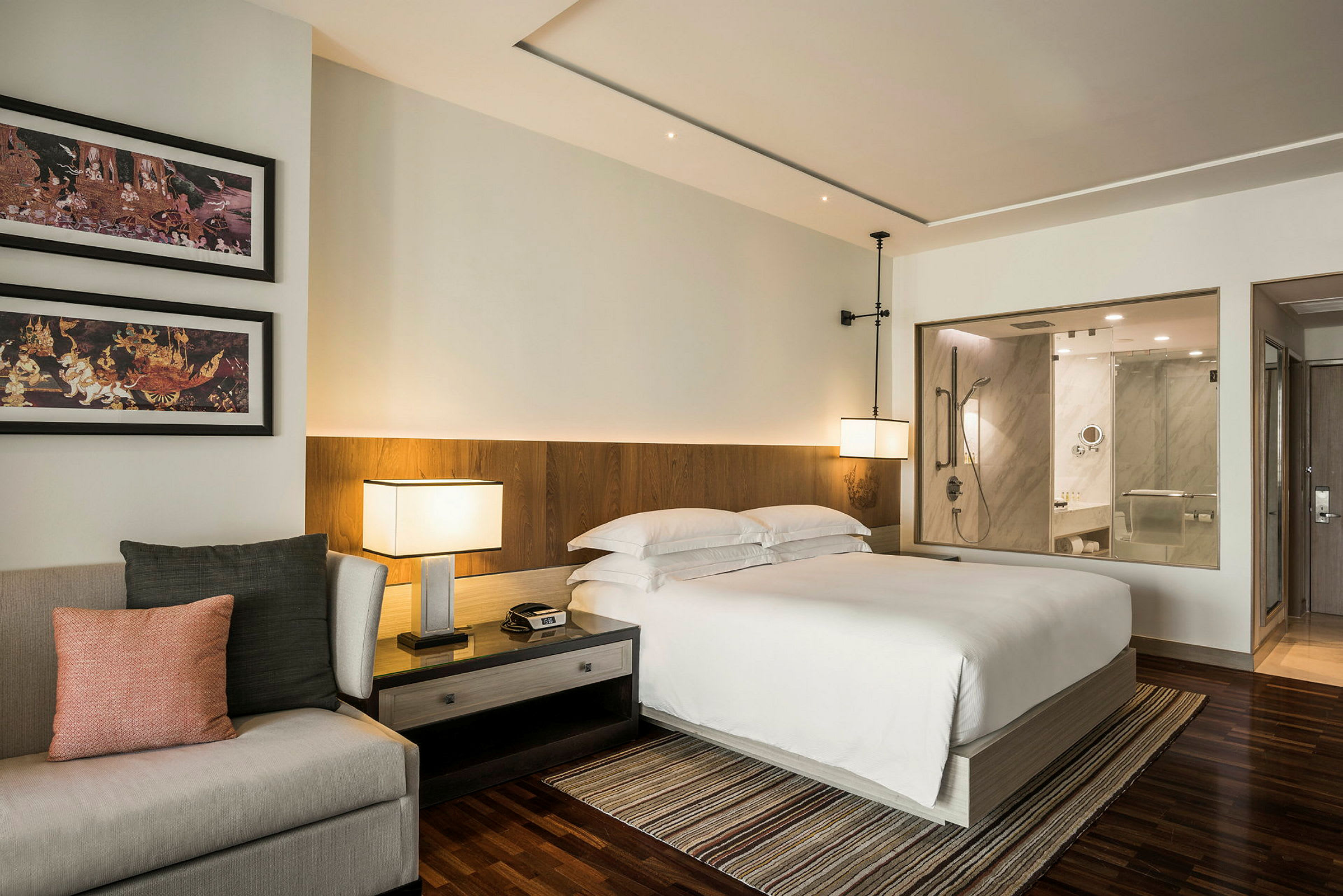 Ett modernt hotellrum med en dubbelsäng, en soffa, nattduksbord och en öppen design som visar ett badrum. (AI-genererad text)