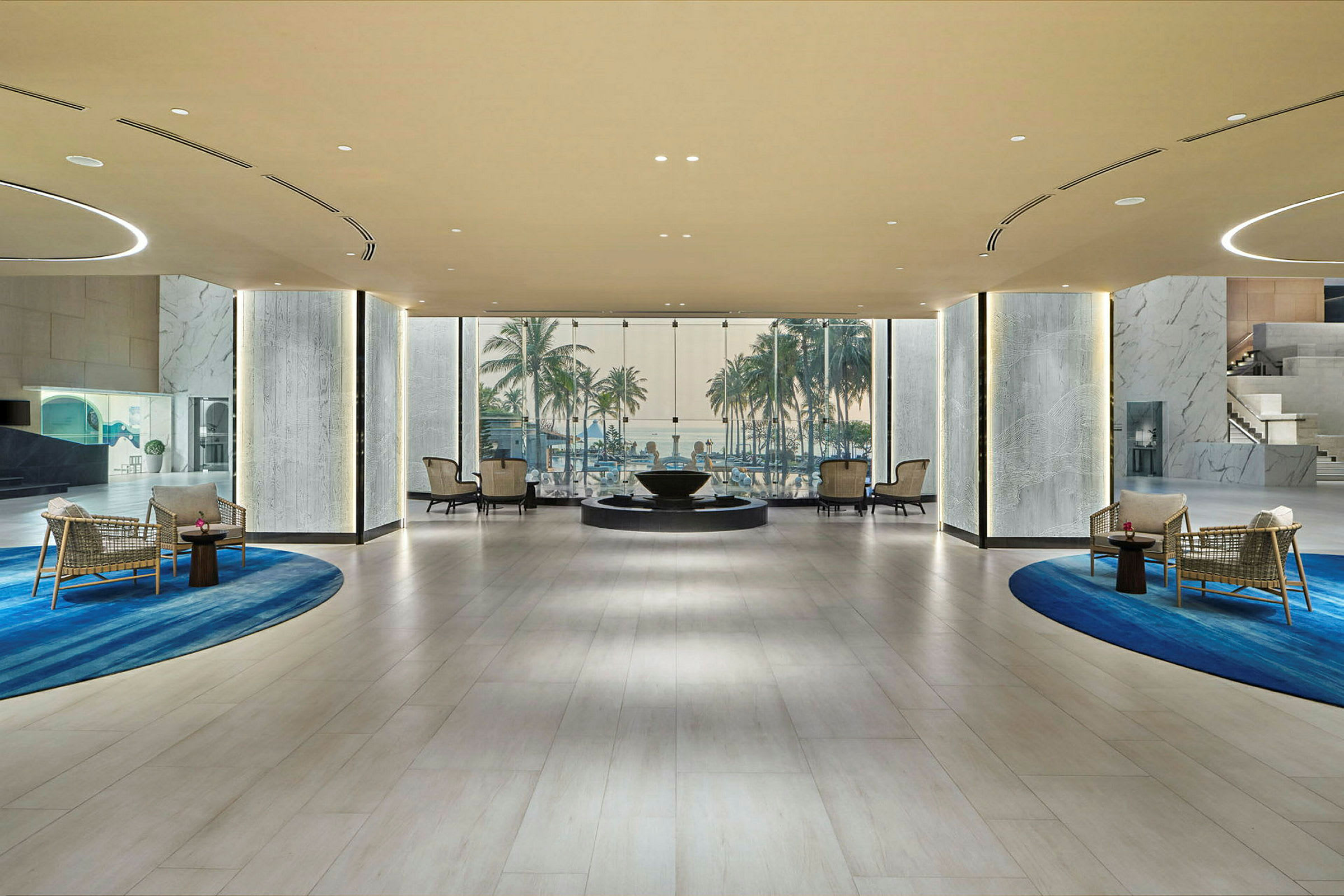 Modernt hotellobby med sittplatser, designade mattor och en bakgrundsutsikt över palmer och himmel genom stora glasrutor. (AI-genererad text)
