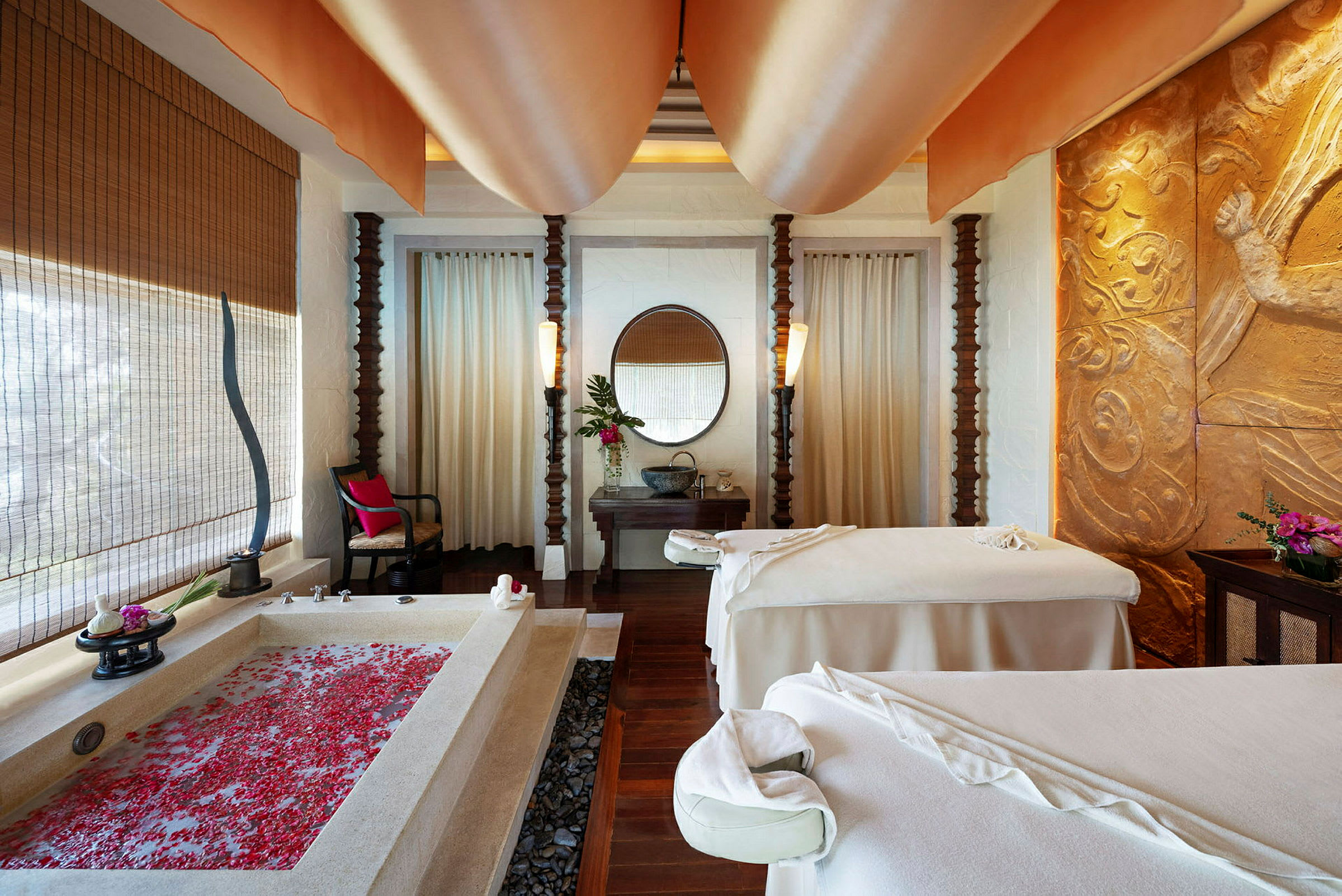 Ett elegant spa-rum med en badkar fylld med rosblad, två massagebänkar och smakfull inredning. (AI-genererad text)