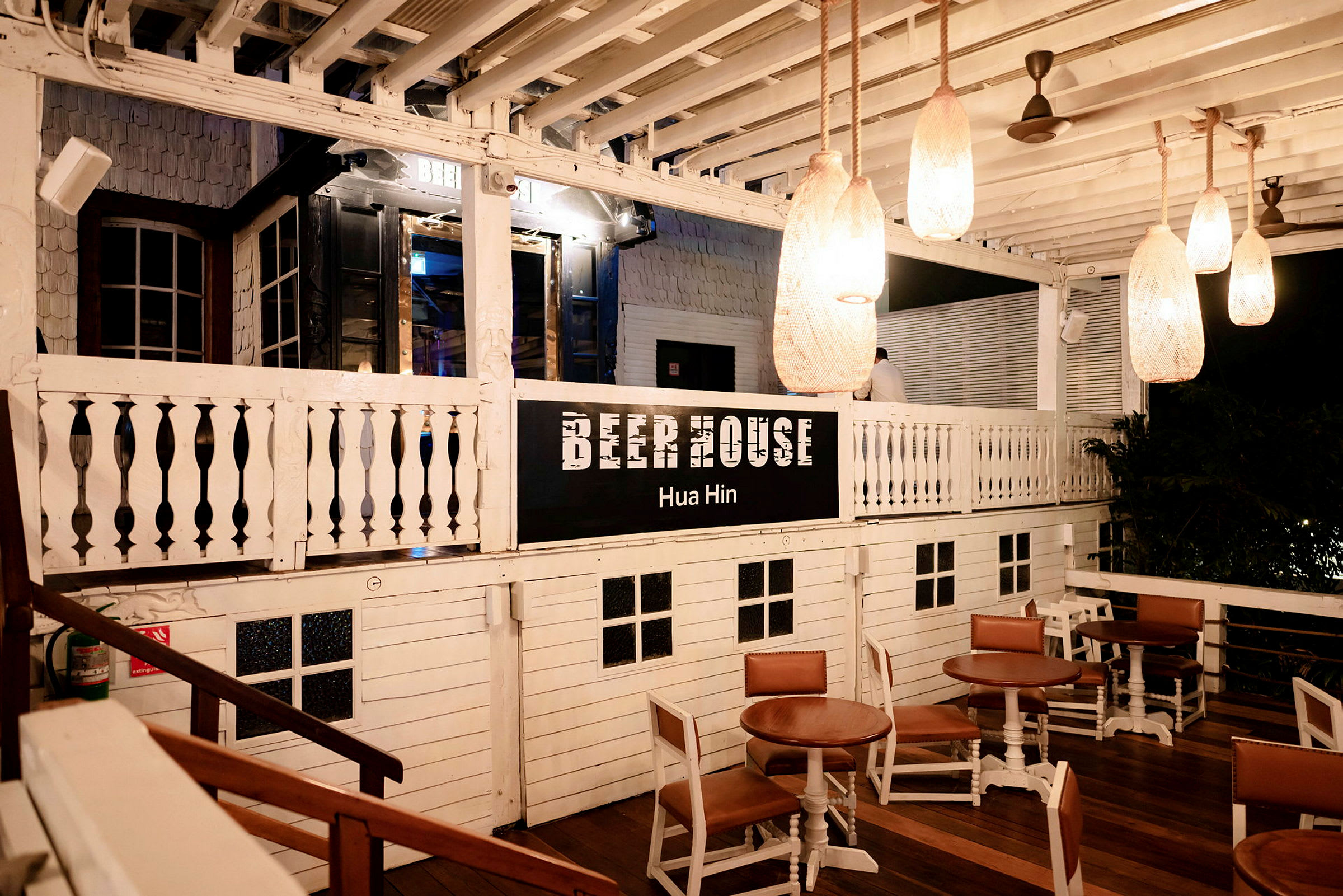 En träbyggnad markerad med texten 'Beer House Hua Hin'. Det finns bord och stolar placerade på en utomhusveranda. (AI-genererad text)