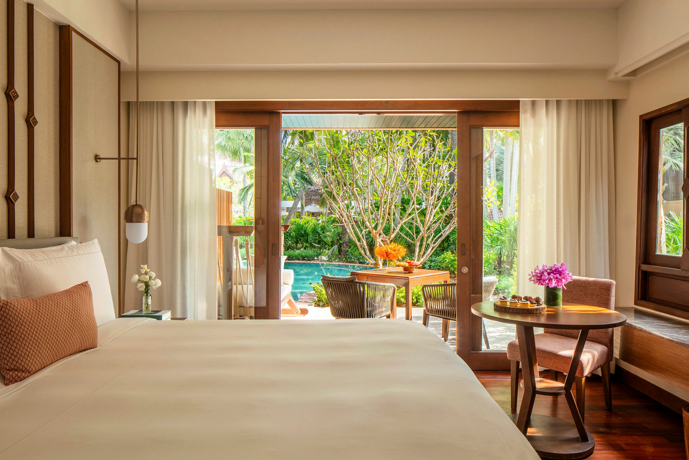 Hotellrum med en stor säng och utsikt mot en trädgård med pool. (AI-genererad text)