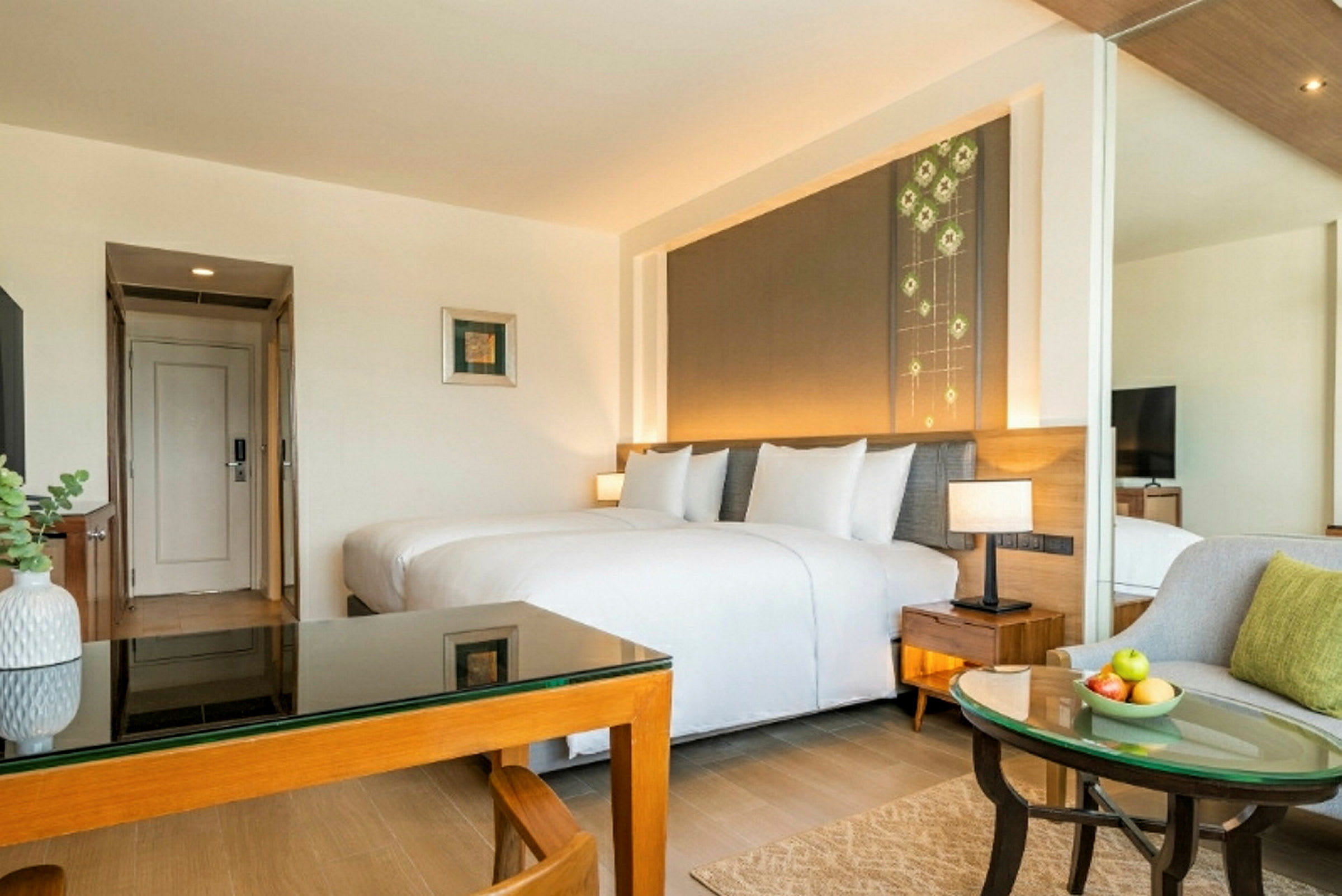 Ett hotellrum med en dubbelsäng, ett glasbord, en stol och en tavla på väggen. Rummet har ljus inredning och ett modernt utseende. (AI-genererad text)