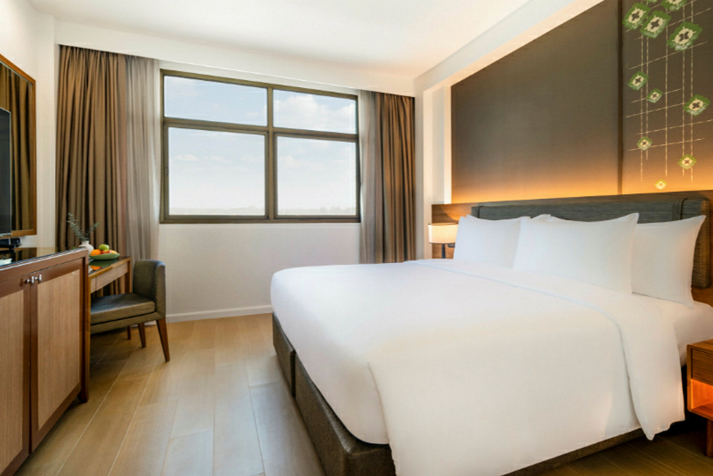 Ett hotellrum med en stor dubbelsäng, ett fönster med beige gardiner och ett skrivbord med en stol och tv. (AI-genererad text)