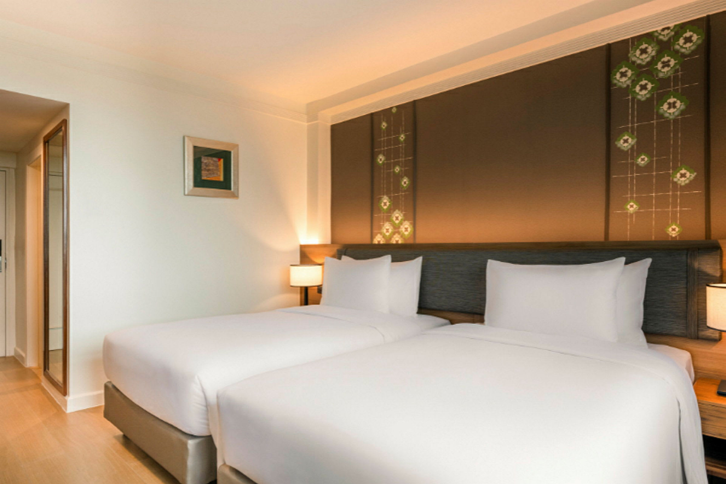 Två bäddar med vita sängkläder i ett hotellrum med väggdekoration och nattbordslampor. (AI-genererad text)