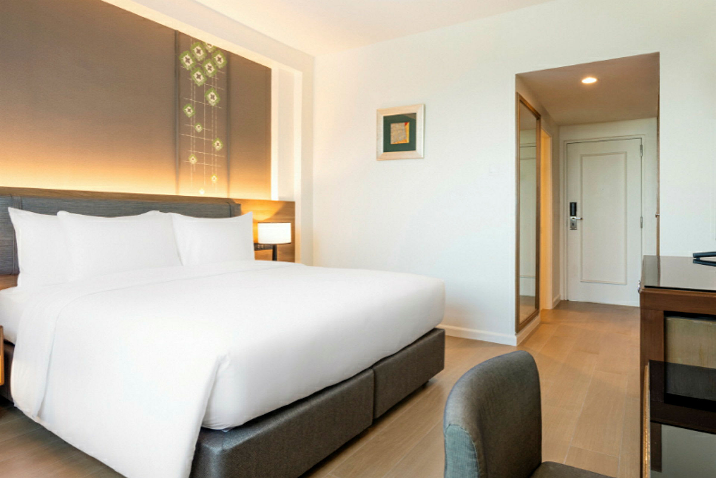 Ett modernt hotellrum med en stor säng klädd i vita lakan och huvudgavel med inbyggd belysning. (AI-genererad text)