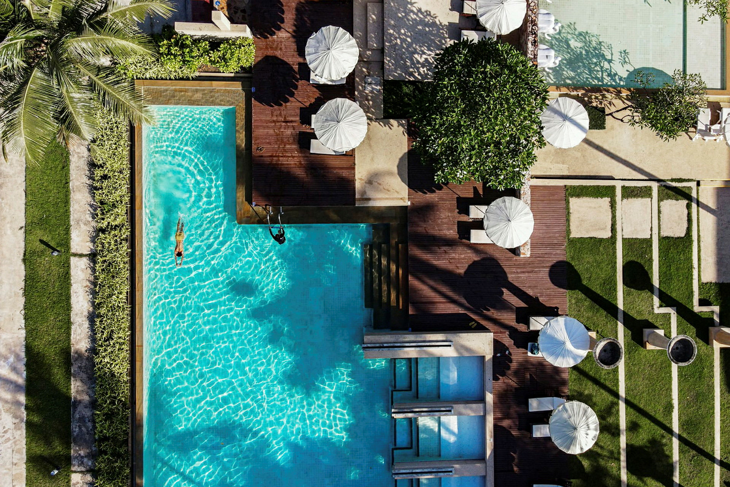 Flygfoto av en swimmingpool med omgivande solstolar och parasoller vid sidan. (AI-genererad text)