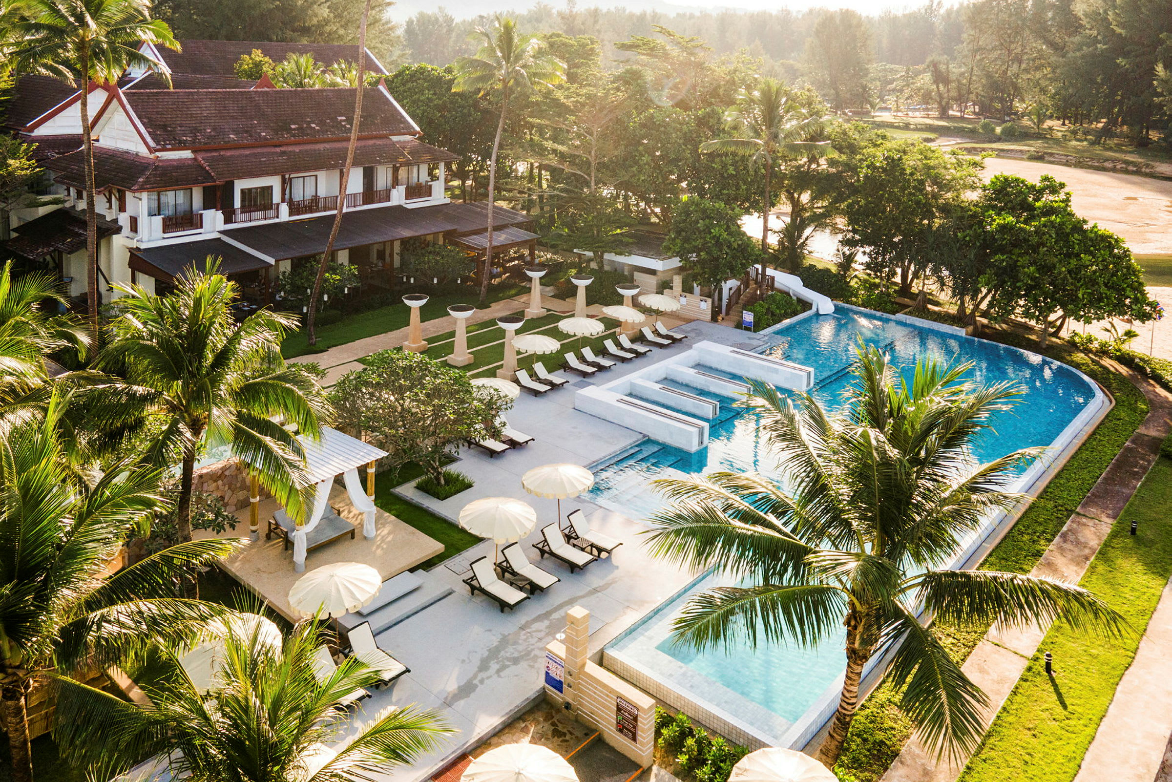 Uppifrån vy över en resort med pool, solstolar och gröna omgivningar. (AI-genererad text)
