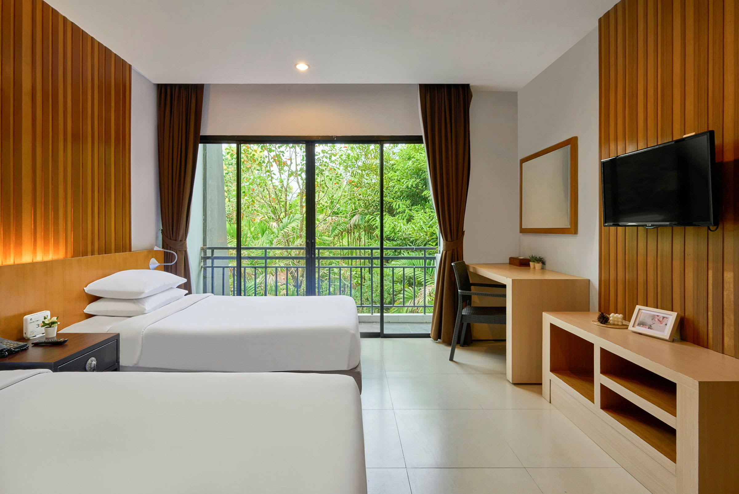 Hotellrum med två enkelsängar, en TV på väggen, skrivbord och stora fönster mot en grönskande utsikt. (AI-genererad text)