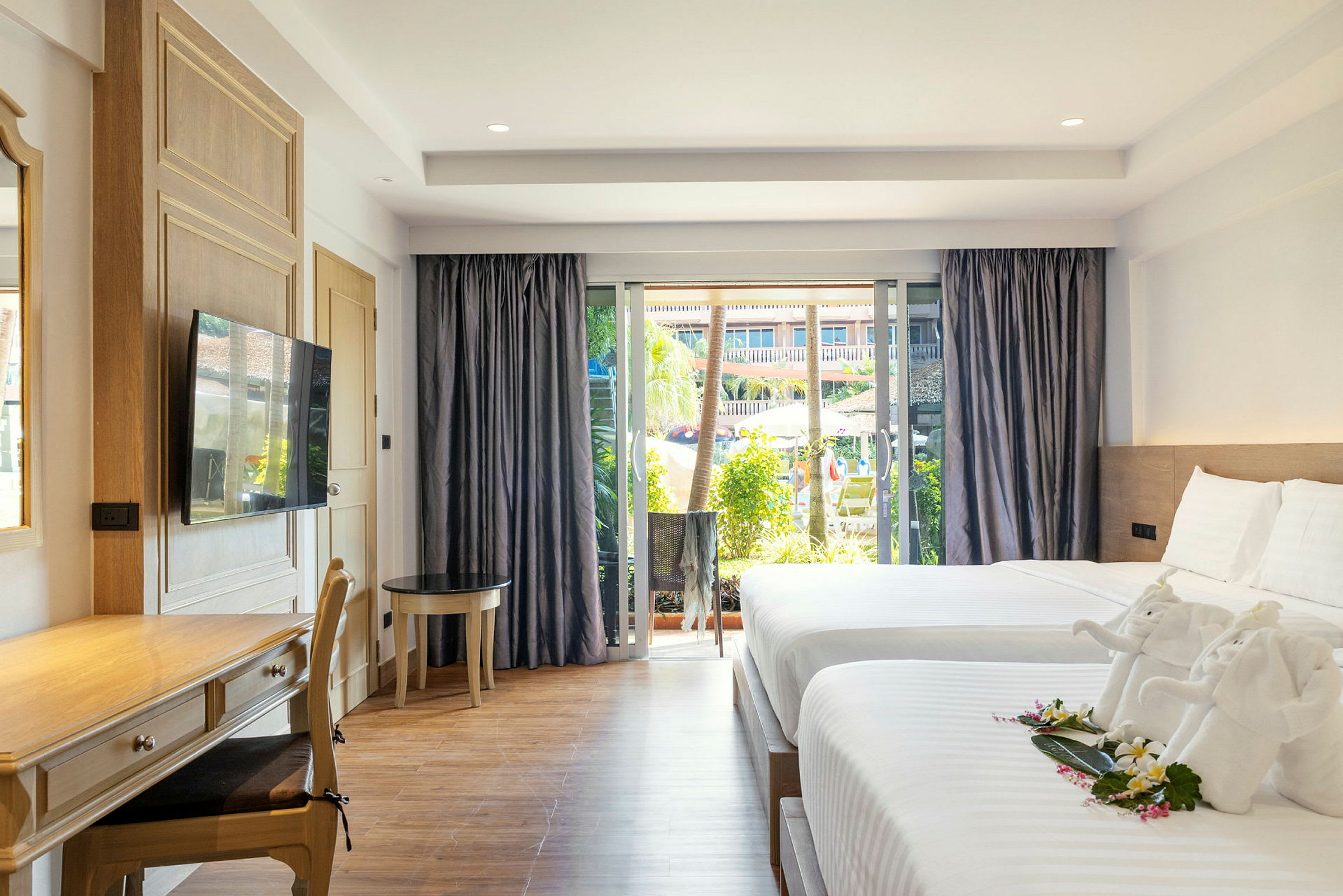 Ett hotellrum med två sängar, en skrivbordshörna och ett stort fönster med utsikt över en pool och trädgård. (AI-genererad text)