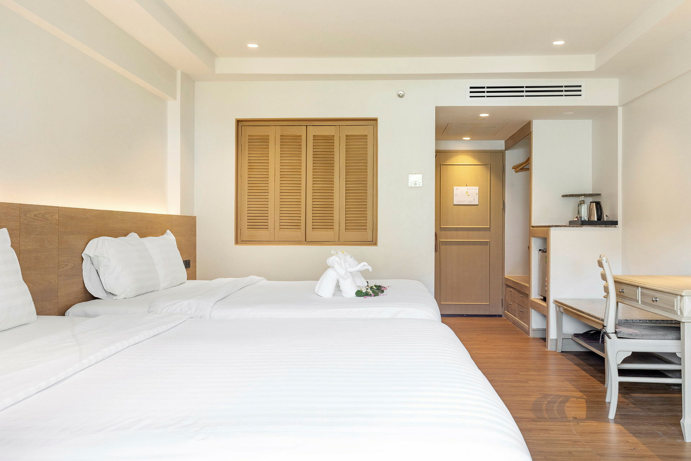 Ett hotellrum med två bäddar, ljusa möbler och ett dekorerat handdukselement på sängen. (AI-genererad text)