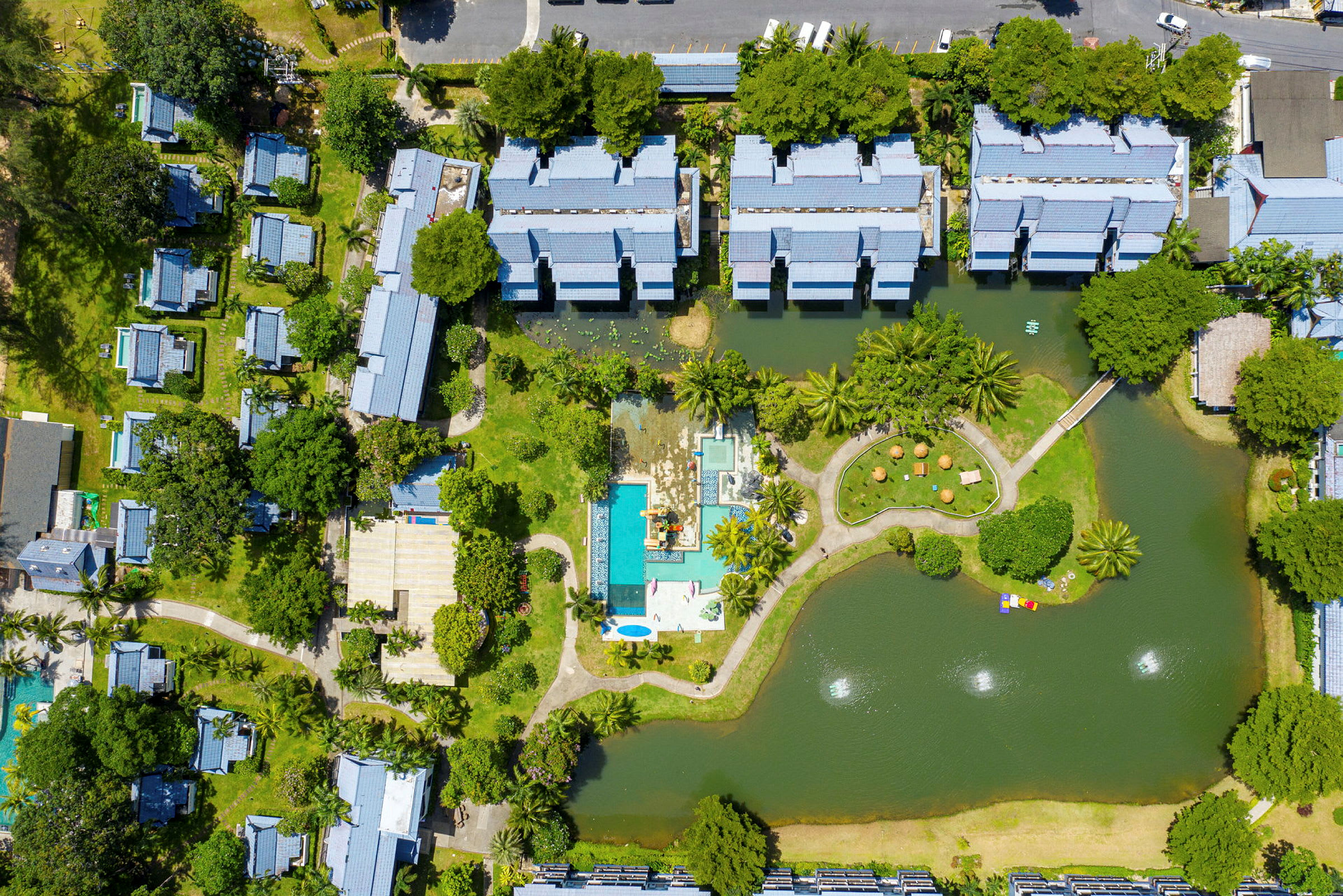 Flygfoto över en resort med byggnader, poolområde och omgivande grönska. (AI-genererad text)