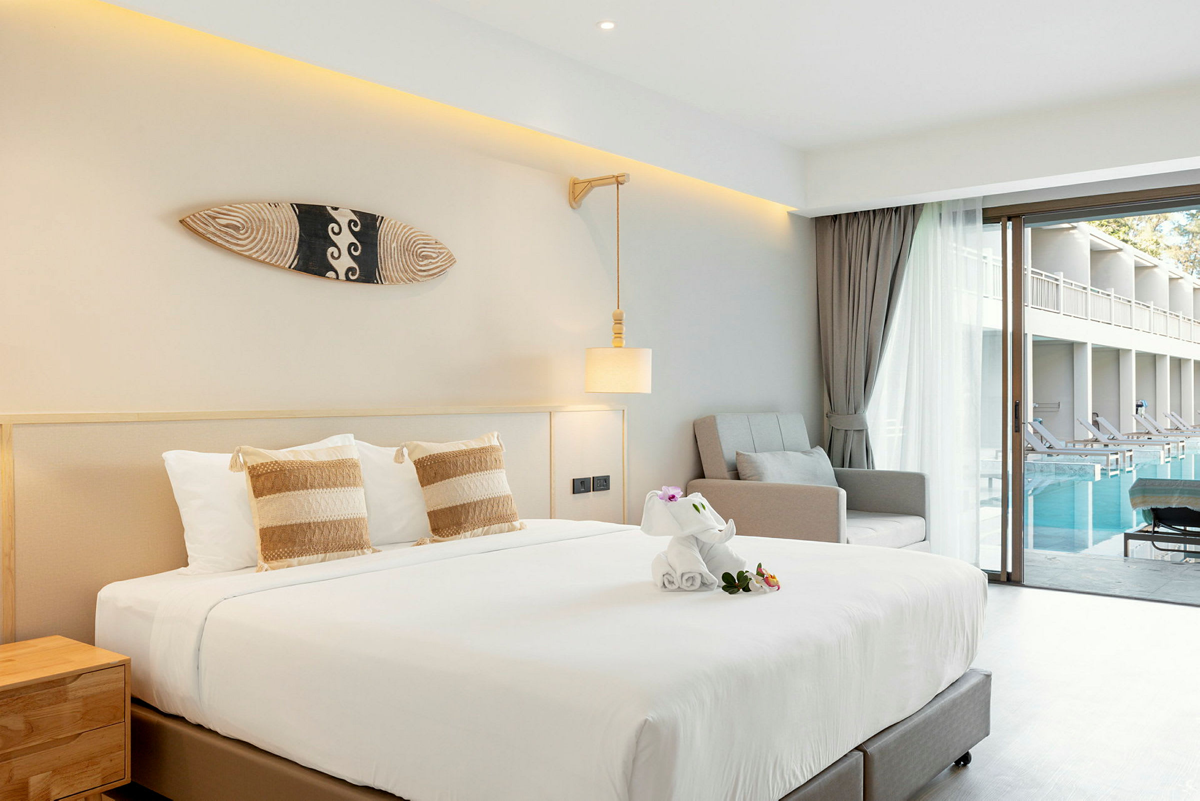 Hotellrum med säng, fåtölj, och utsikt över pool från en glasdörr. (AI-genererad text)