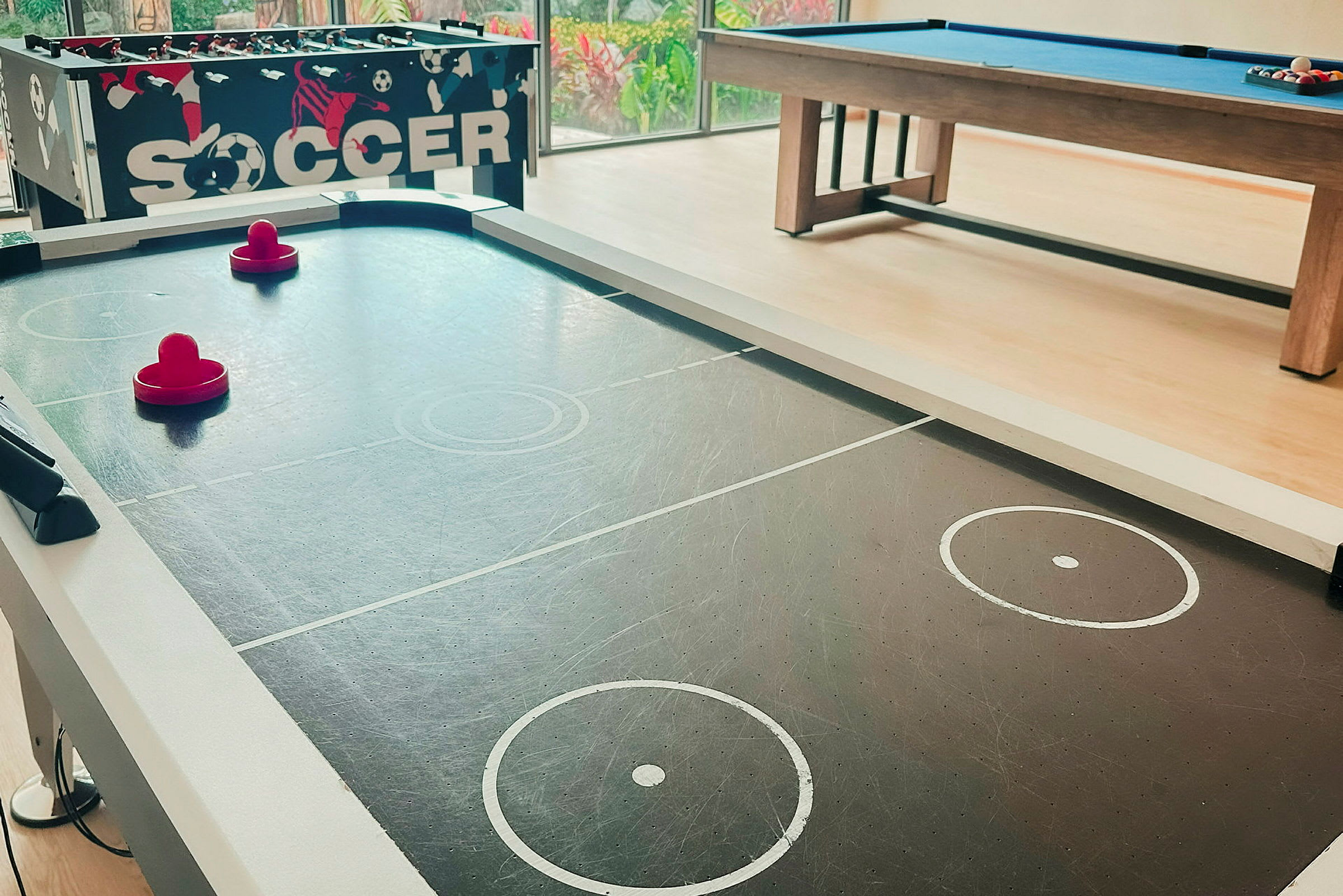 Ett luftshockeybord med två röda paddlar och en biljardbord i bakgrunden. (AI-genererad text)