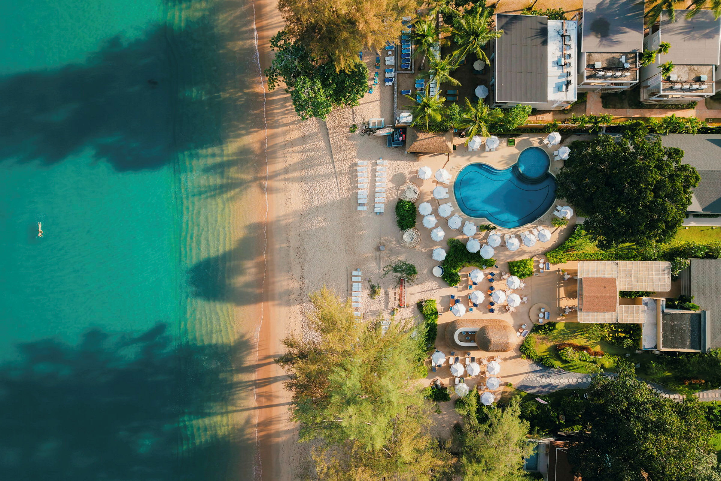 Flygbild över en strand och en resort med pool och parasoller. (AI-genererad text)