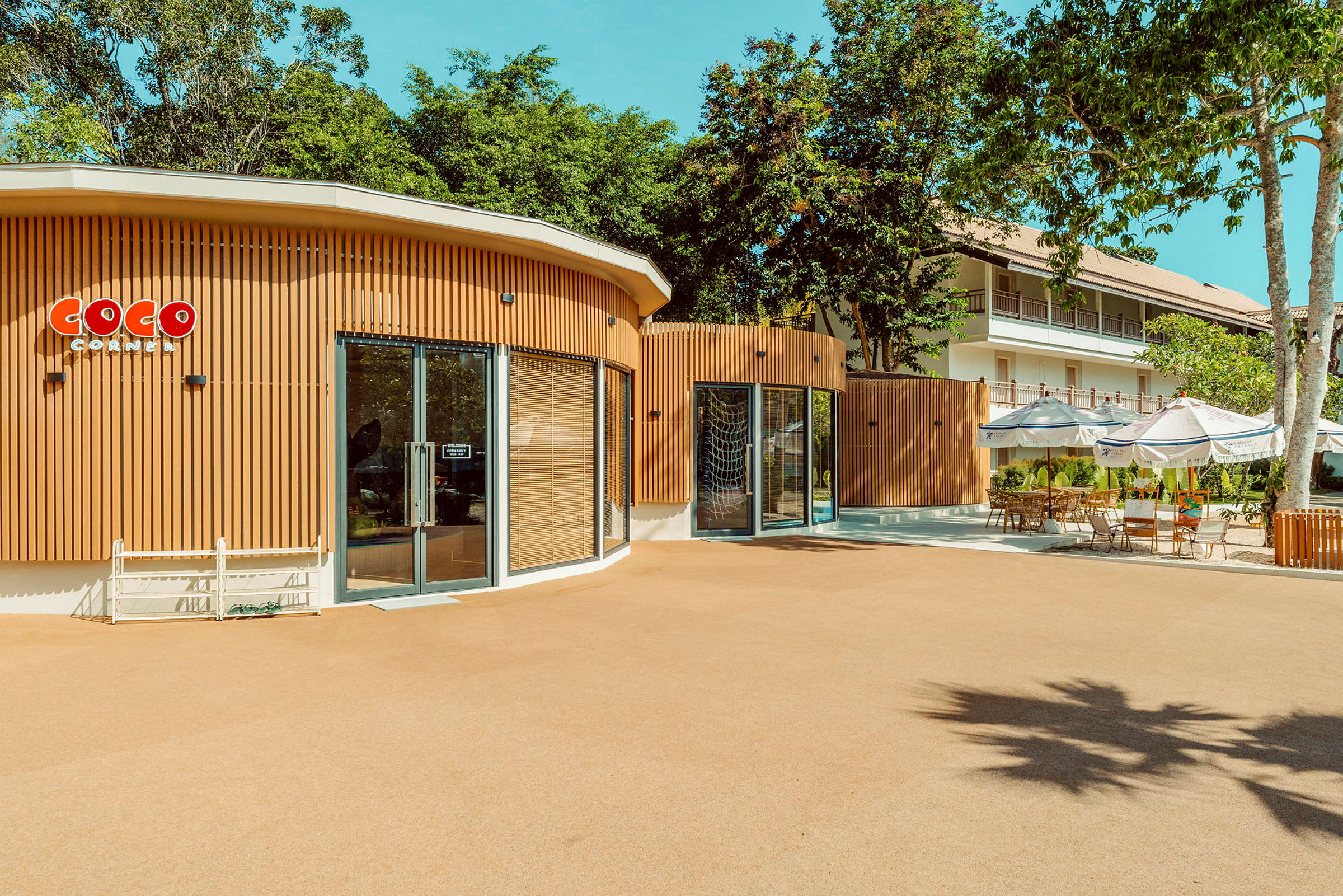En byggnad med en skylt som säger 'Coco Corner' och omgivande träd och utemöbler. (AI-genererad text)