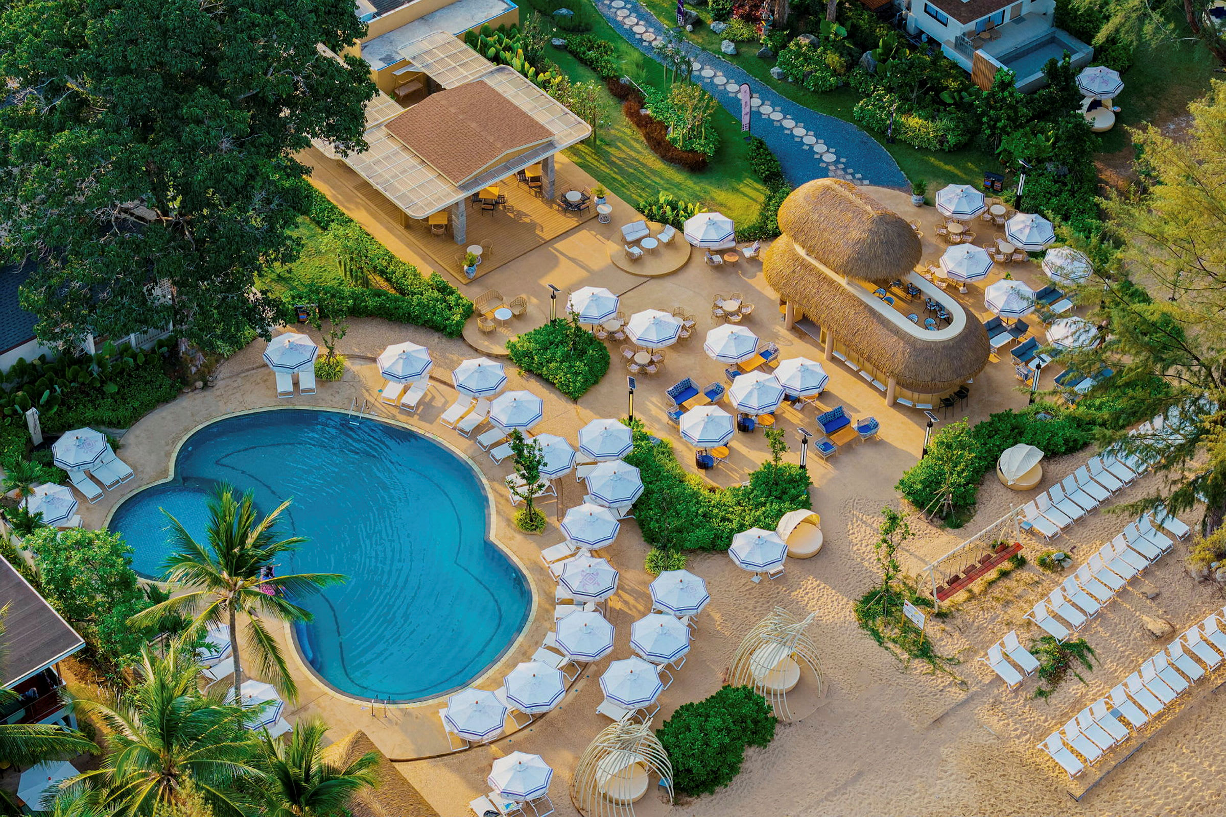 Flygfoto över en resort med pool, solstolar och parasoller i en tropisk miljö. (AI-genererad text)
