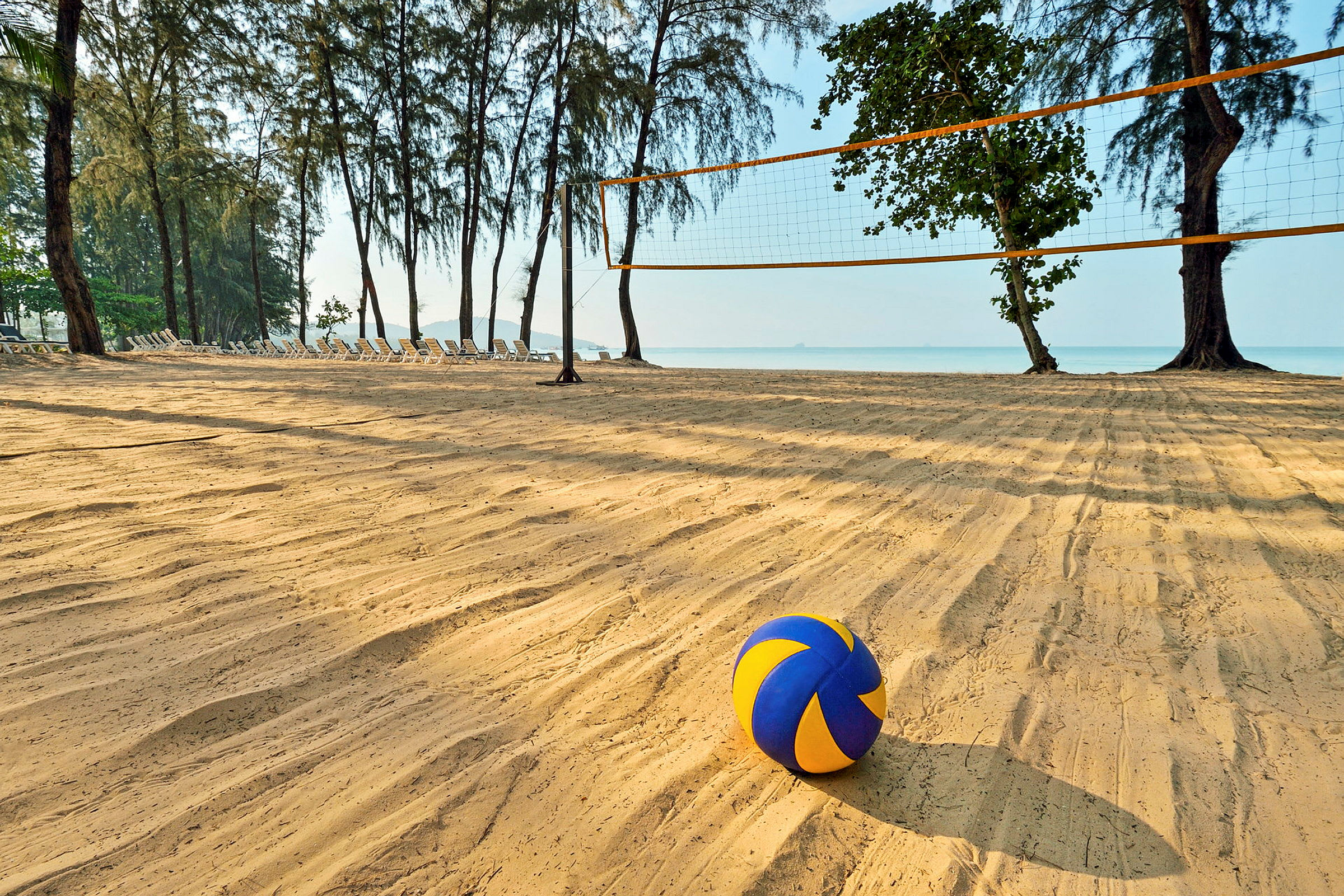 En strand med ett volleybollnät och en färgglad volleyboll i förgrunden. (AI-genererad text)