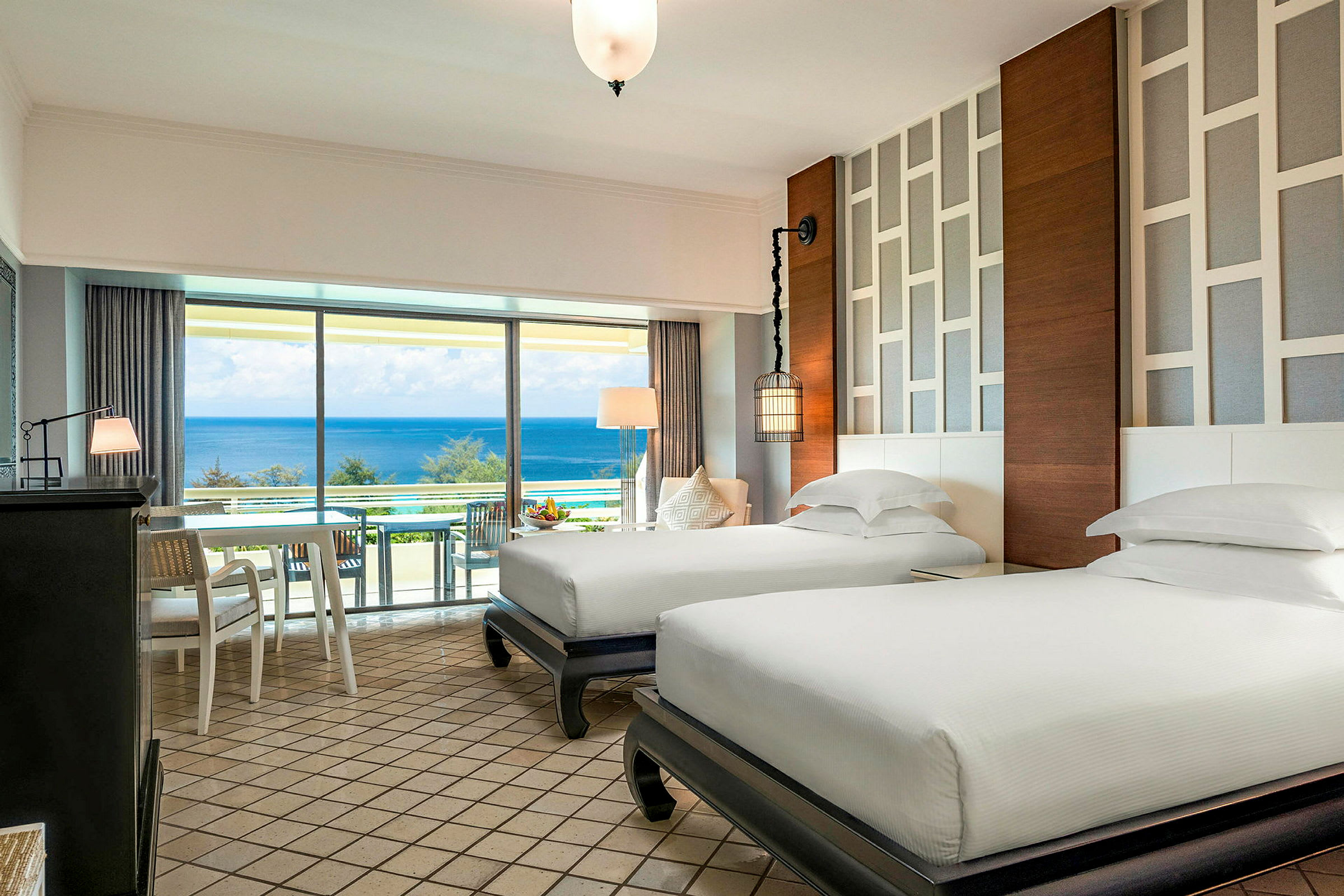 Ett hotellrum med två separata enkelsängar, moderna möbler och en ljus design. Ett stort fönster med utsikt över havet. (AI-genererad text)