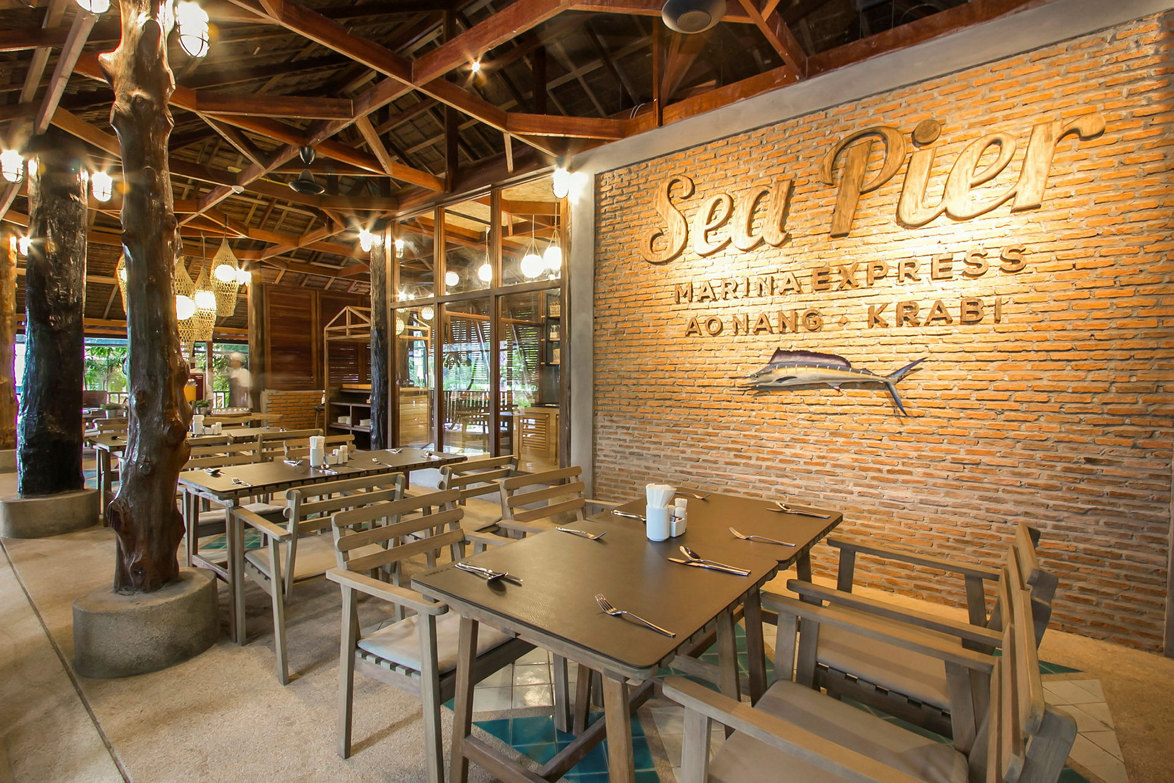 En rustik restaurang med träbord och stolar, insida med tegelvägg dekorerad med texten 'Sea Pier' och fiskmotiv. (AI-genererad text)