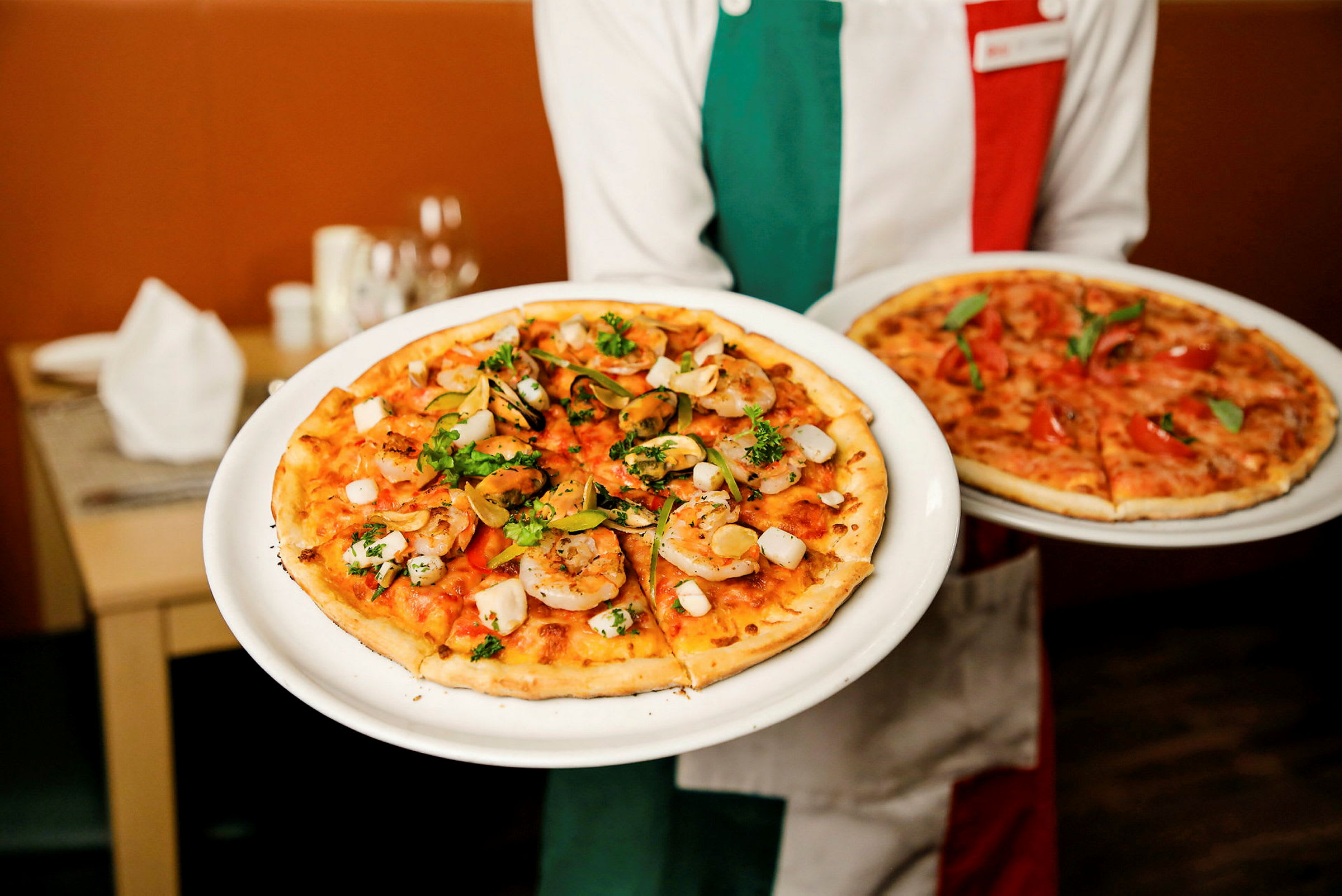 En person håller två tallrikar med pizzor, varav en har räkor och örter som topping. (AI-genererad text)
