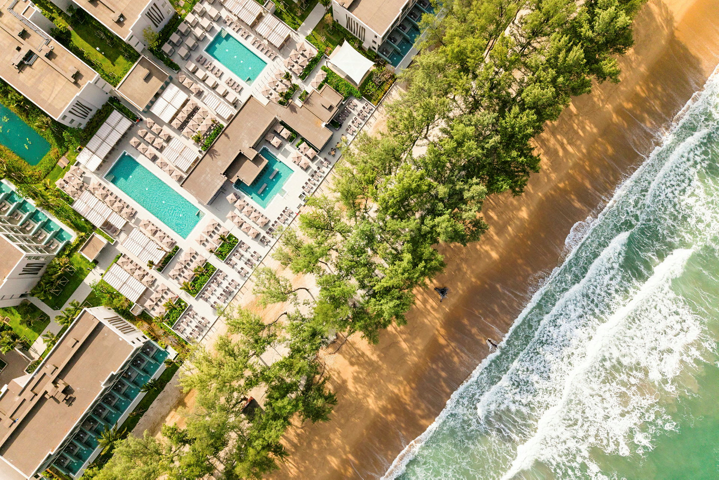 Flygbild av en lyxig resort som ligger intill en strand med vågor och träd i förgrunden. (AI-genererad text)