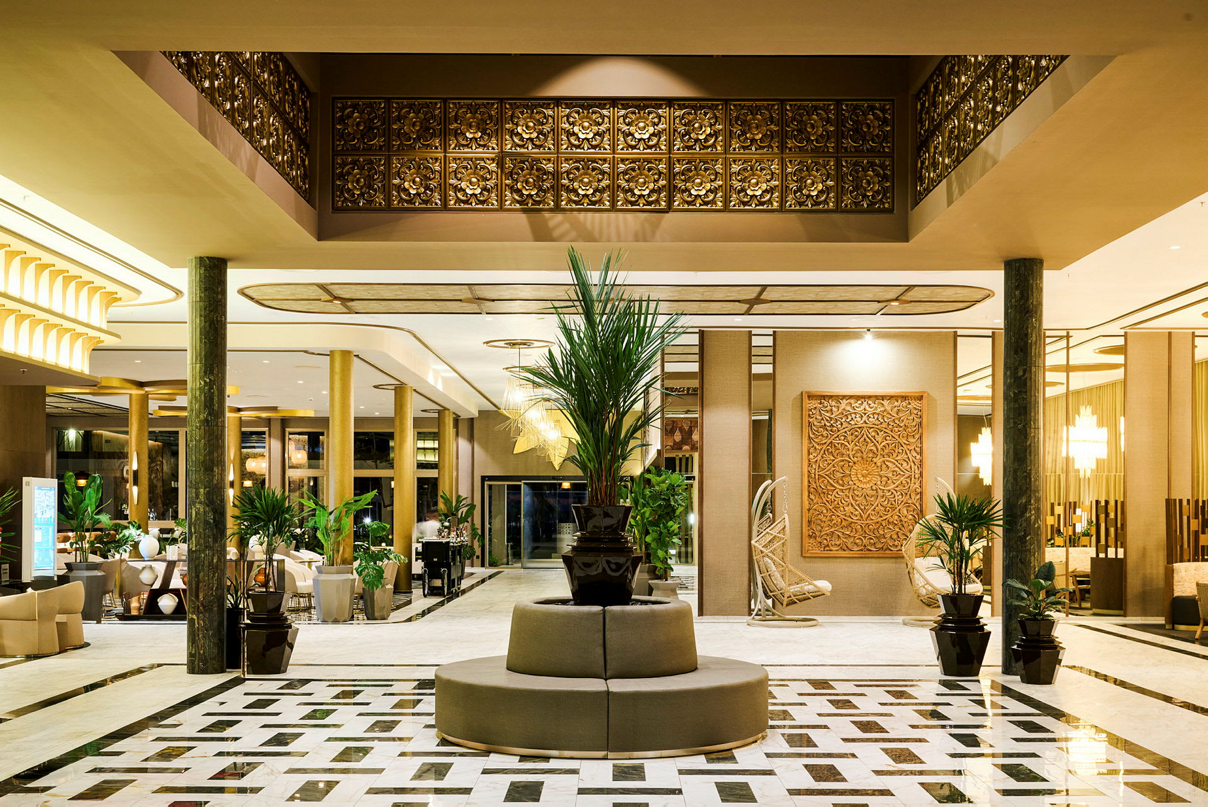 En elegant hotellobby med marmorgolv, dekorationer i guld och trä och växter placerade runt området. (AI-genererad text)