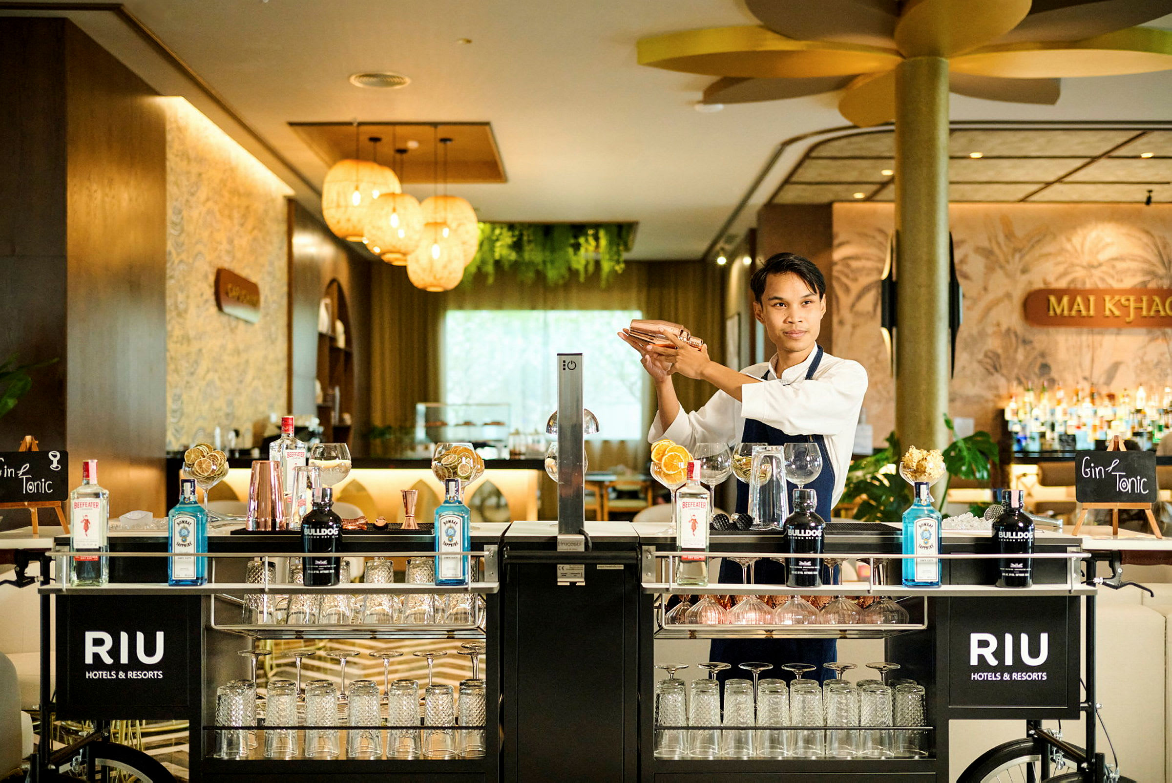 En bartender blandar en drink vid en välutrustad barvagn i en elegant hotellmiljö. (AI-genererad text)