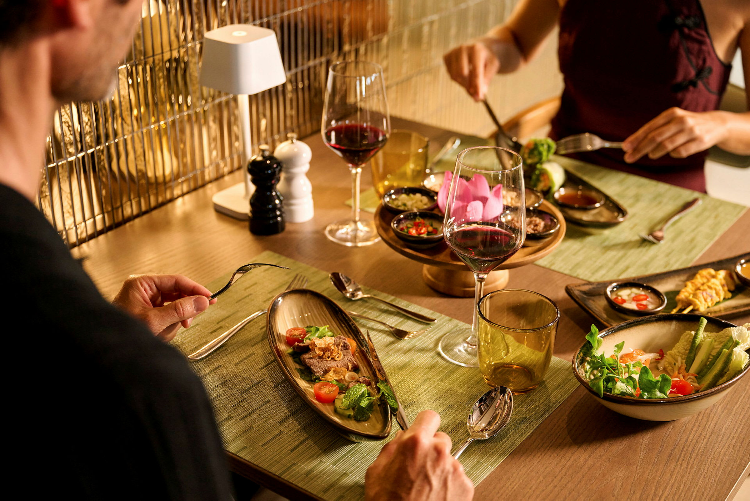 Två personer sitter vid ett bord med eleganta tallrikar och glas med vin, omgivna av smakfullt upplagda rätter. (AI-genererad text)
