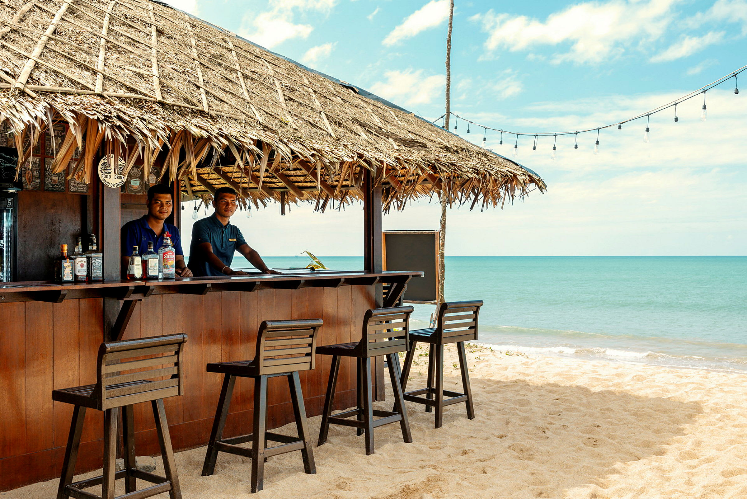 Strandbar med halmtak och hav i bakgrunden. (AI-genererad text)
