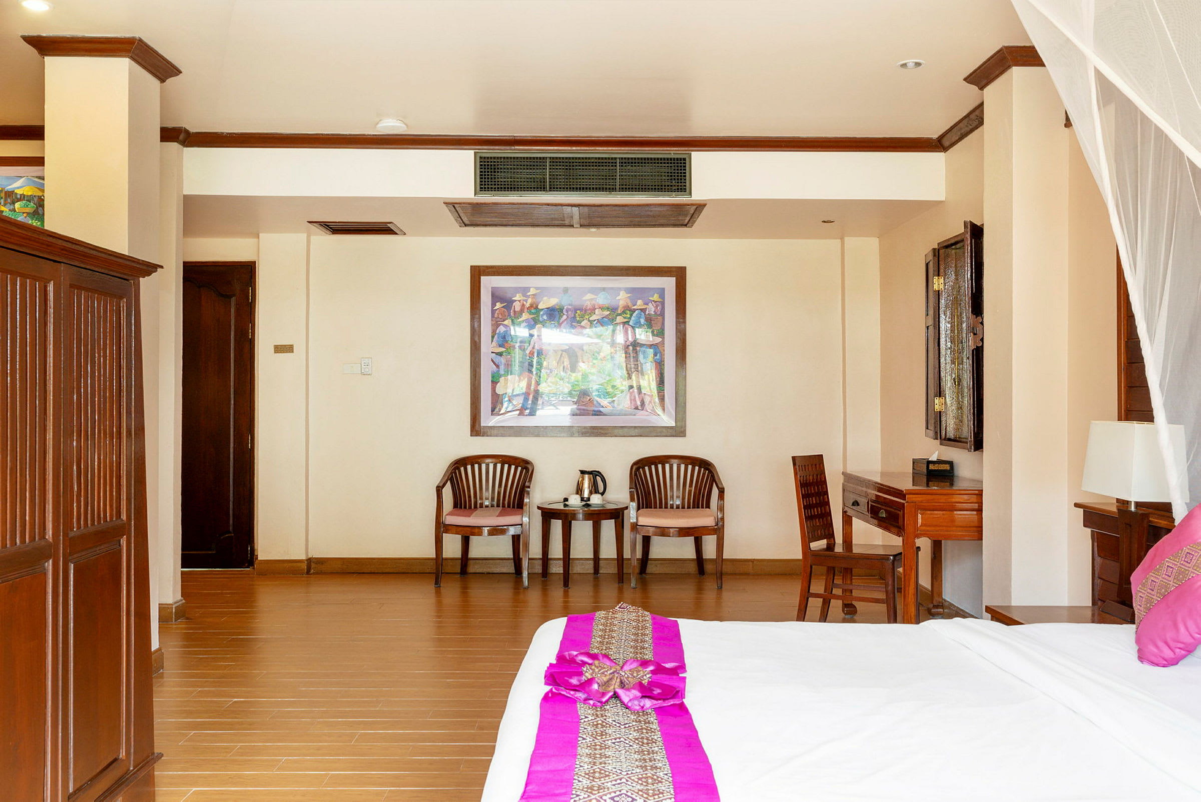 Ett hotellrum med ljusa väggar, träinredning och en stor säng med rosa dekorativa inslag. (AI-genererad text)