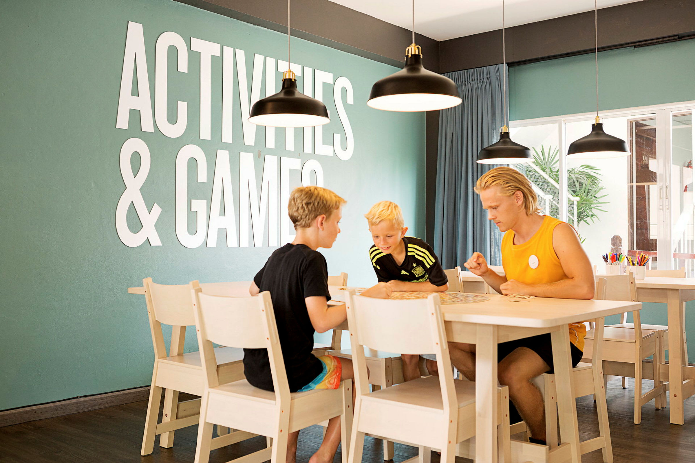 Personer spelar ett bordsspel vid ett bord i ett rum med texten "Activities & Games" på väggen. (AI-genererad text)